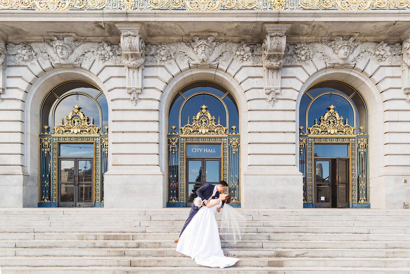 wide shot of the exterior of SF City HAll with couple dip-kissing