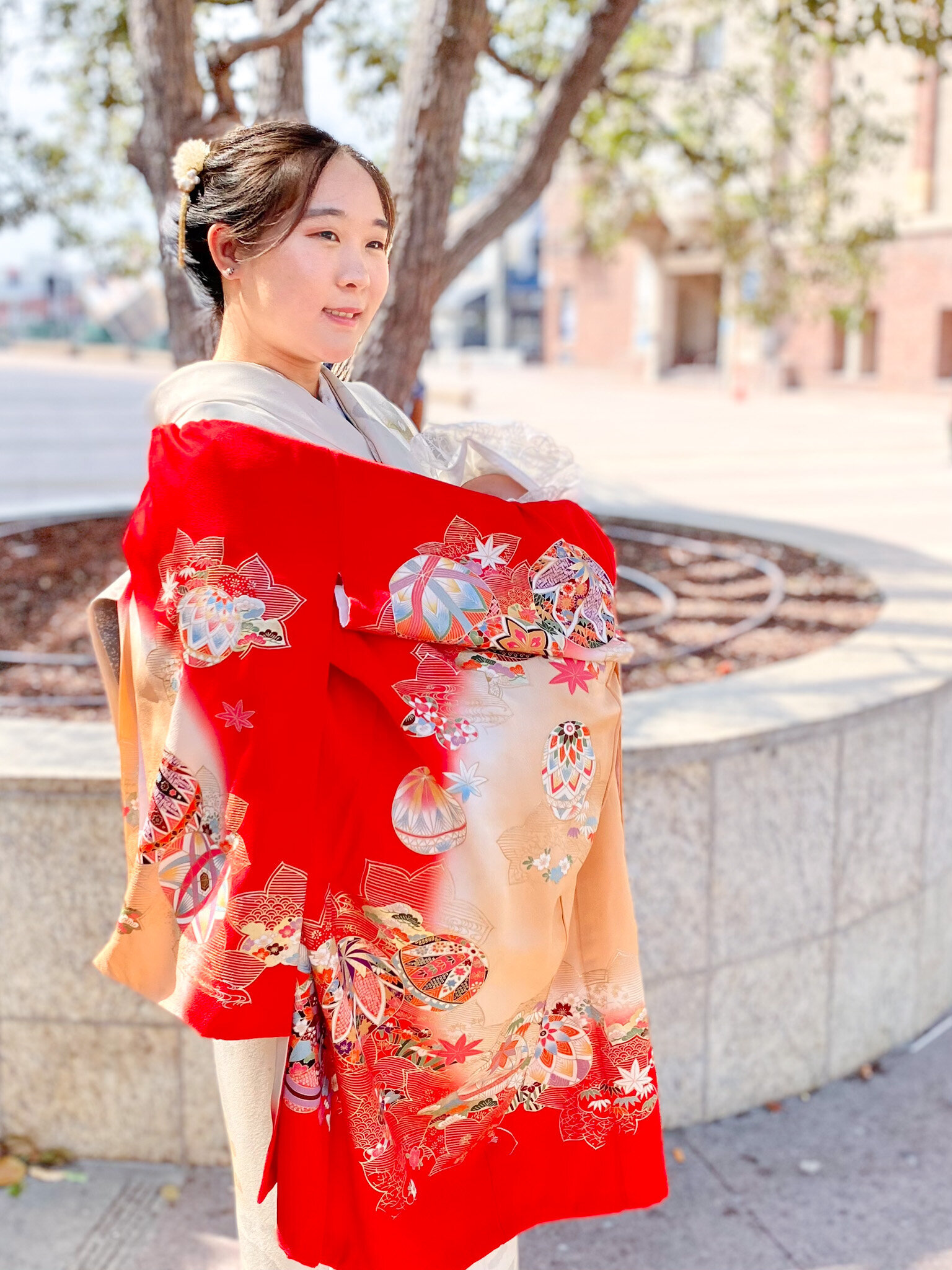 Mother wearing vibrant red kimono holding baby during Hatsumairi ceremony outdoors | 初参り 母 赤い着物 赤ちゃん 屋外 ロサンゼルス