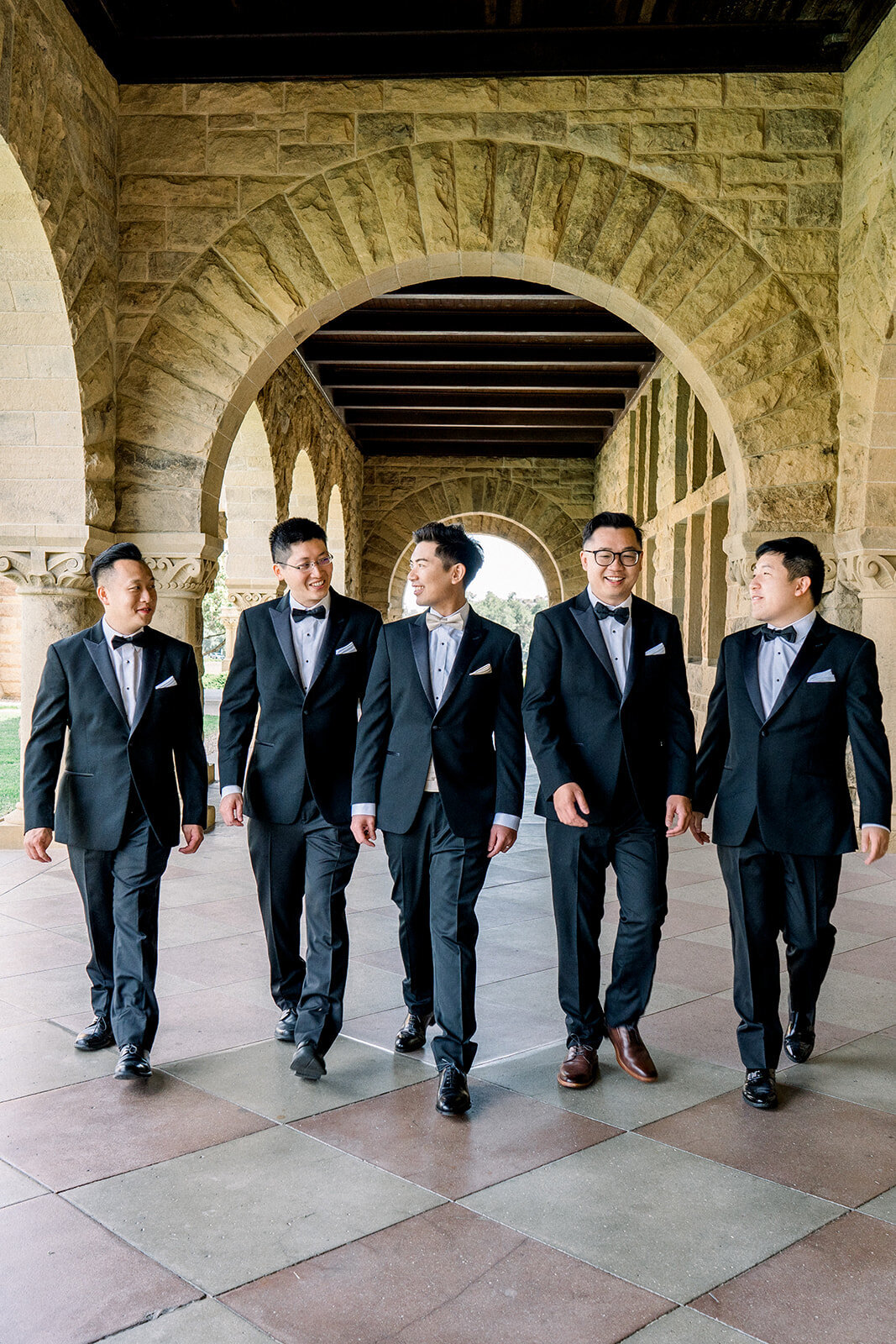 The groomsmen walk confidently under the historic arches of Stanford University, capturing a moment of camaraderie and style.