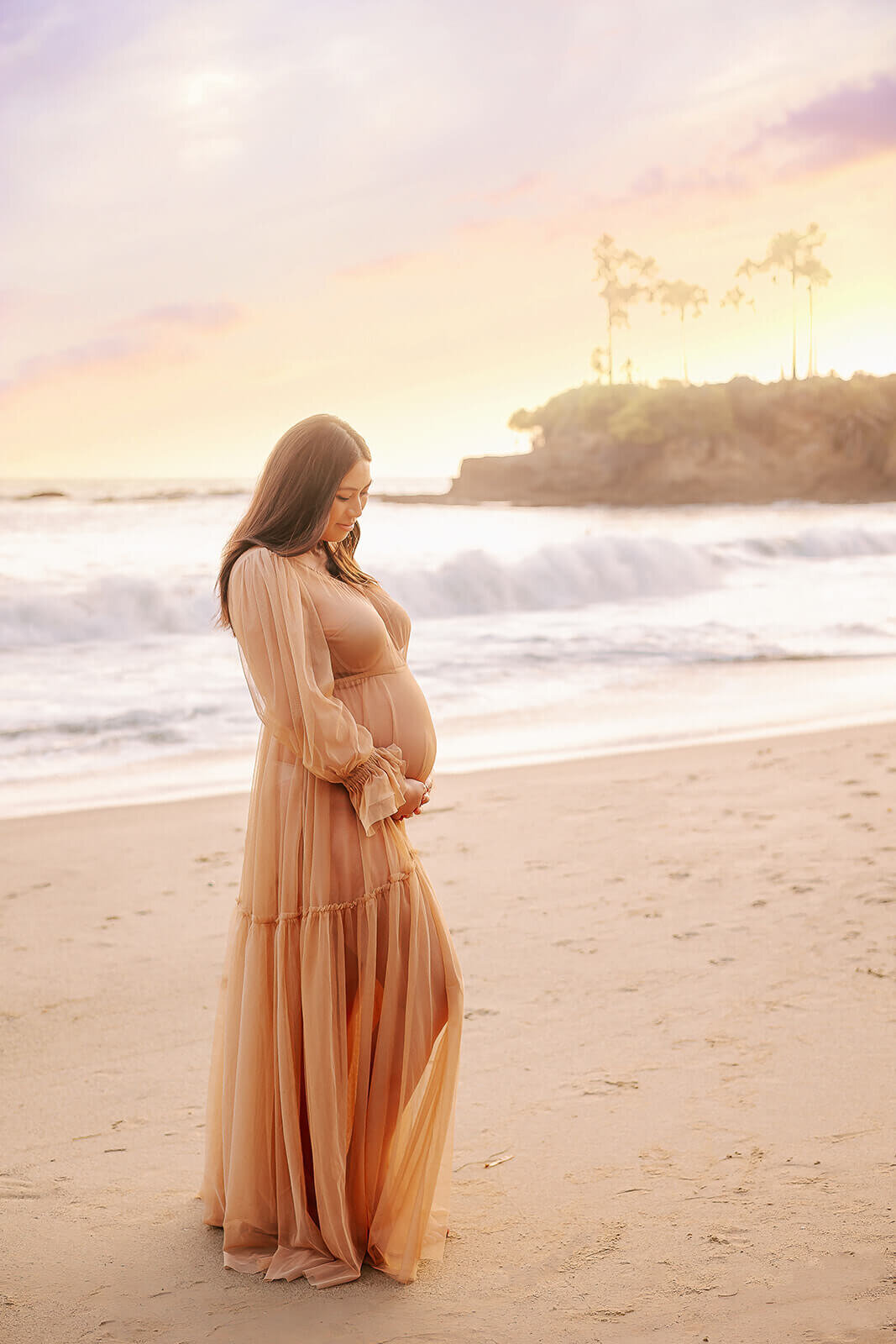 Expectant Mom standing on beach looking down at baby bump in Laguna Beach by Ashley Nicole.