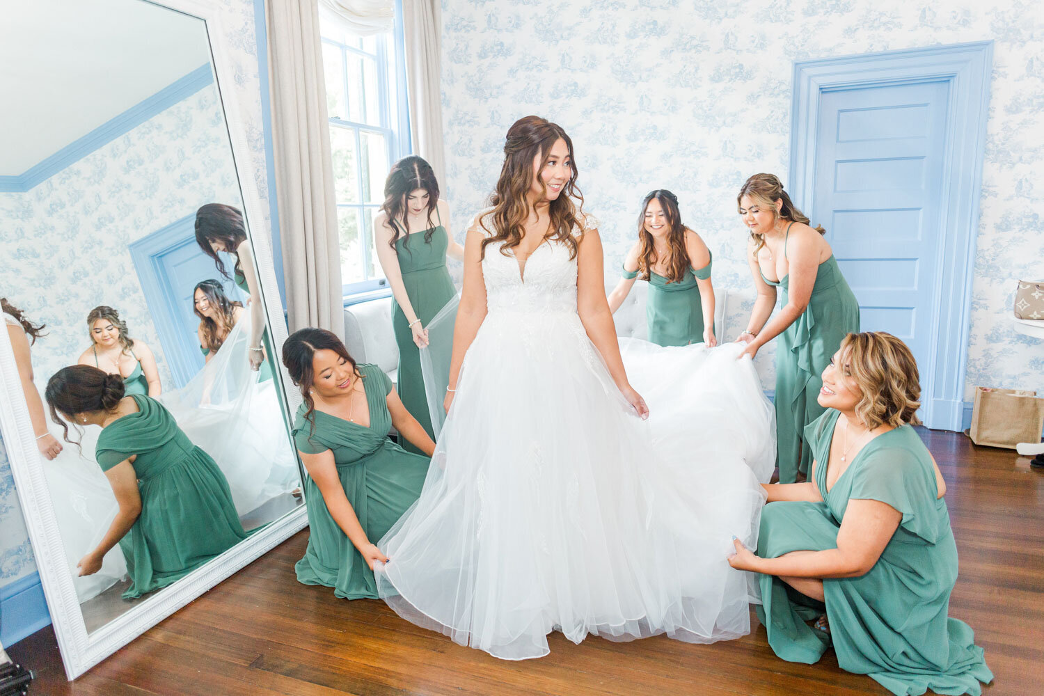 Bride in white gown with bridesmaids in green dresses adjusting train