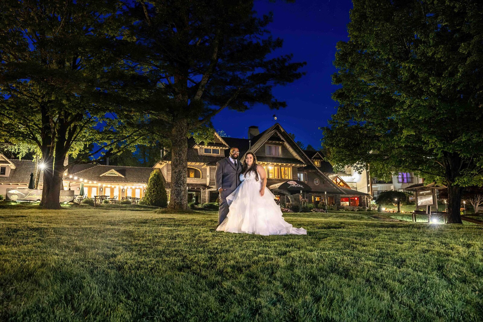 The bride and groom stand together under the stars on a glowing lawn at a mountain wedding venue, Chetola Resort, in Blowing Rock, NC, showcasing rustic elegance and a romantic nighttime setting.