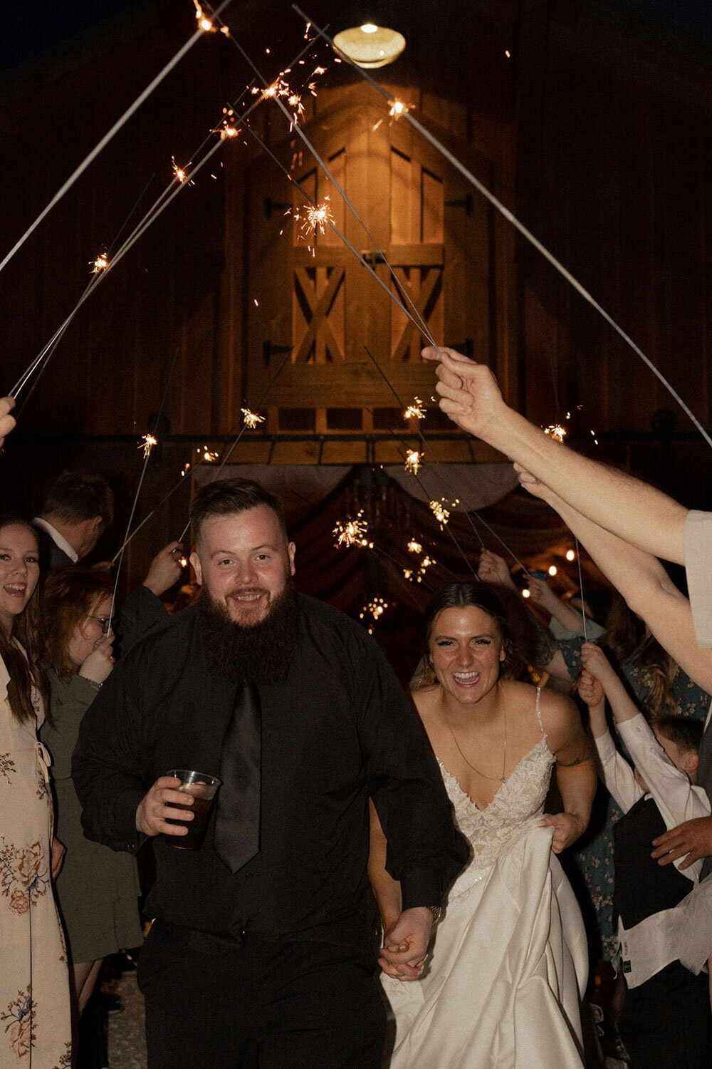 Bride and groom running through a sparkler exit with joyful expressions