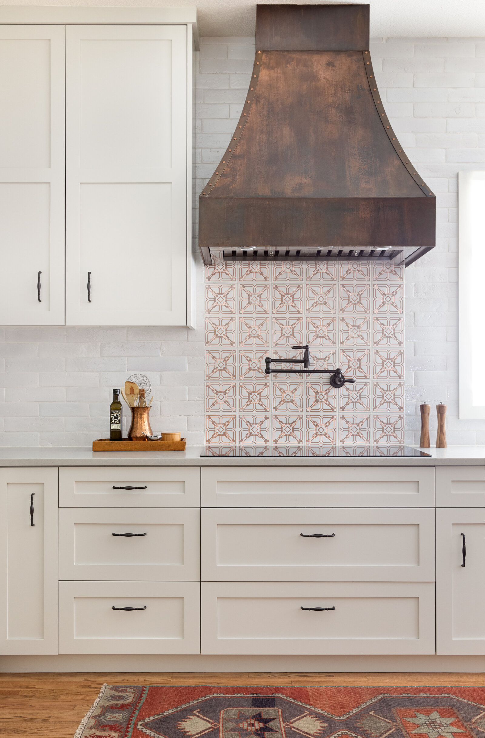 beige colored kitchen with aztec orange and white backsplash with a custom steel vent hood