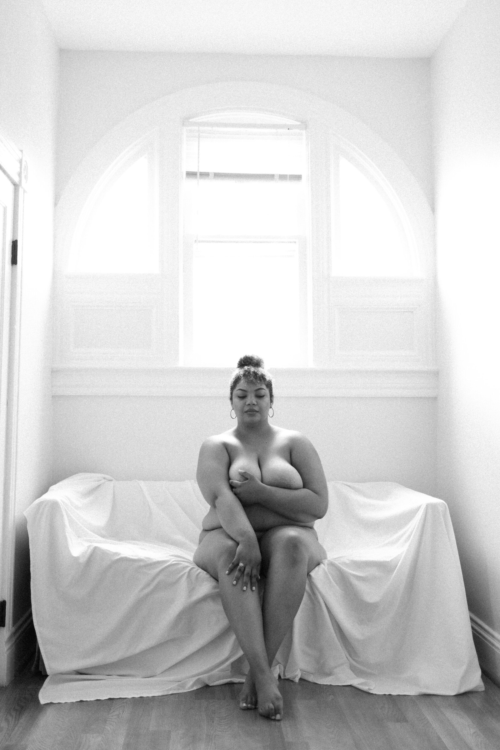 Black and white boudoir photo of woman sitting on a bed