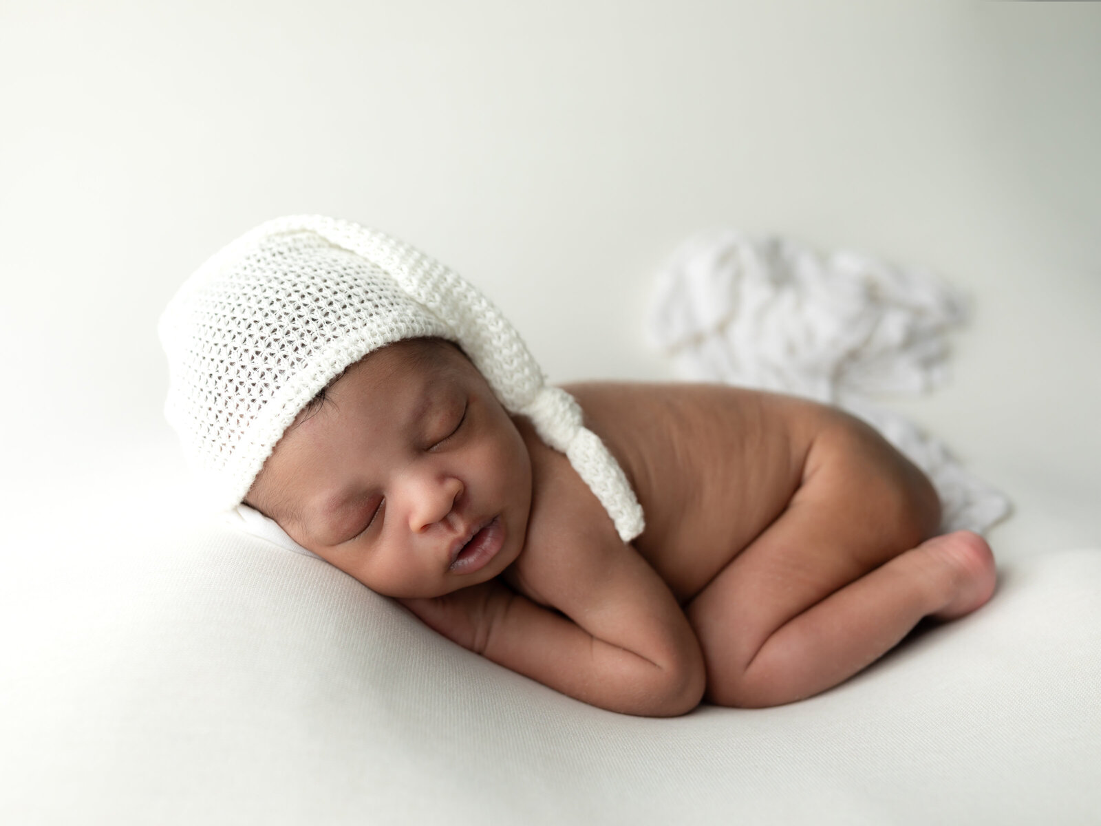 newborn baby boy in white hat posed on white fabric for studio newborn portraits cleveland newborn photographer