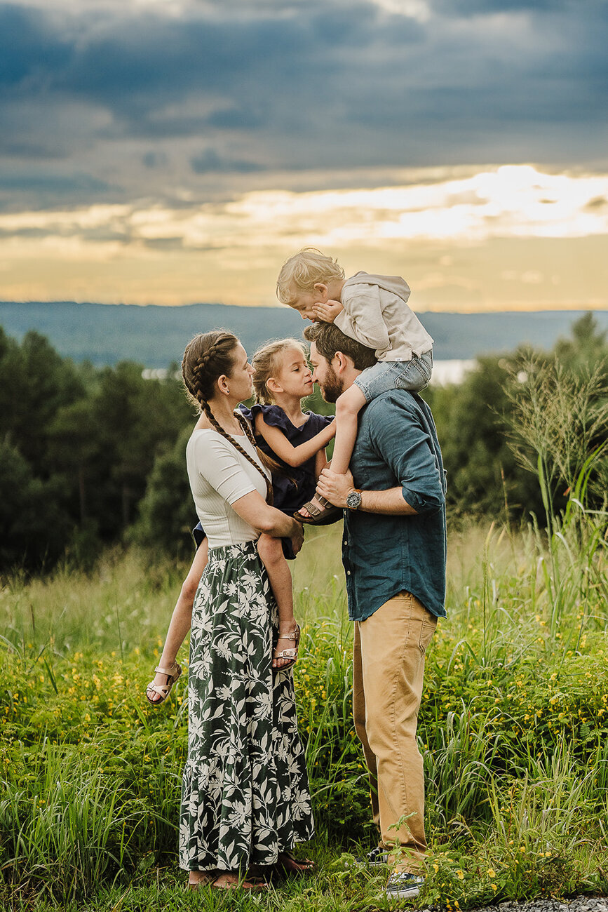 family stands with two children in a field under dramatic sunset sky