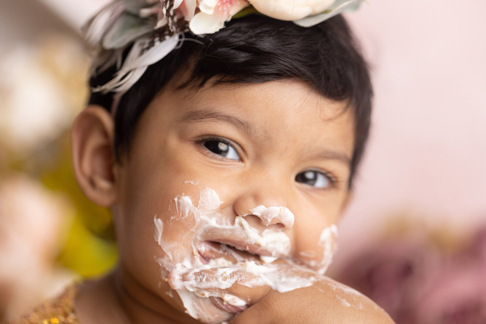 Close up of girls face covered in icing at cake smash.