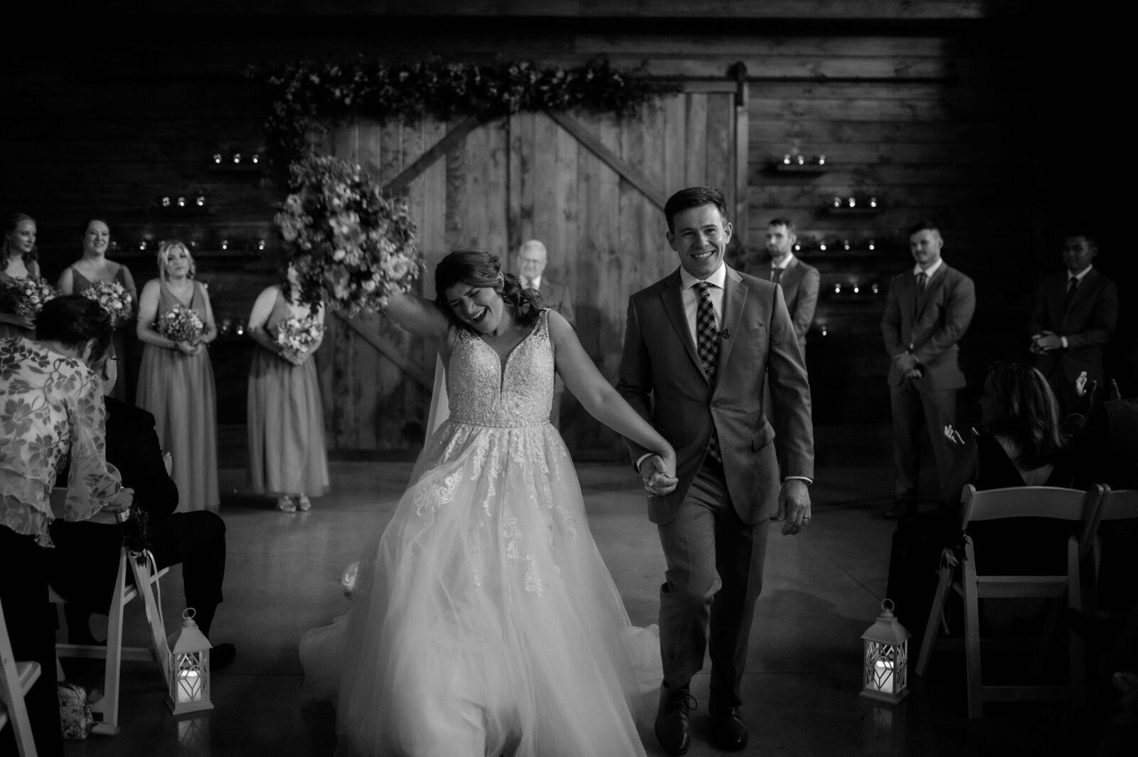 couple exiting wedding ceremony in rustic barn holding hands, bride cheering