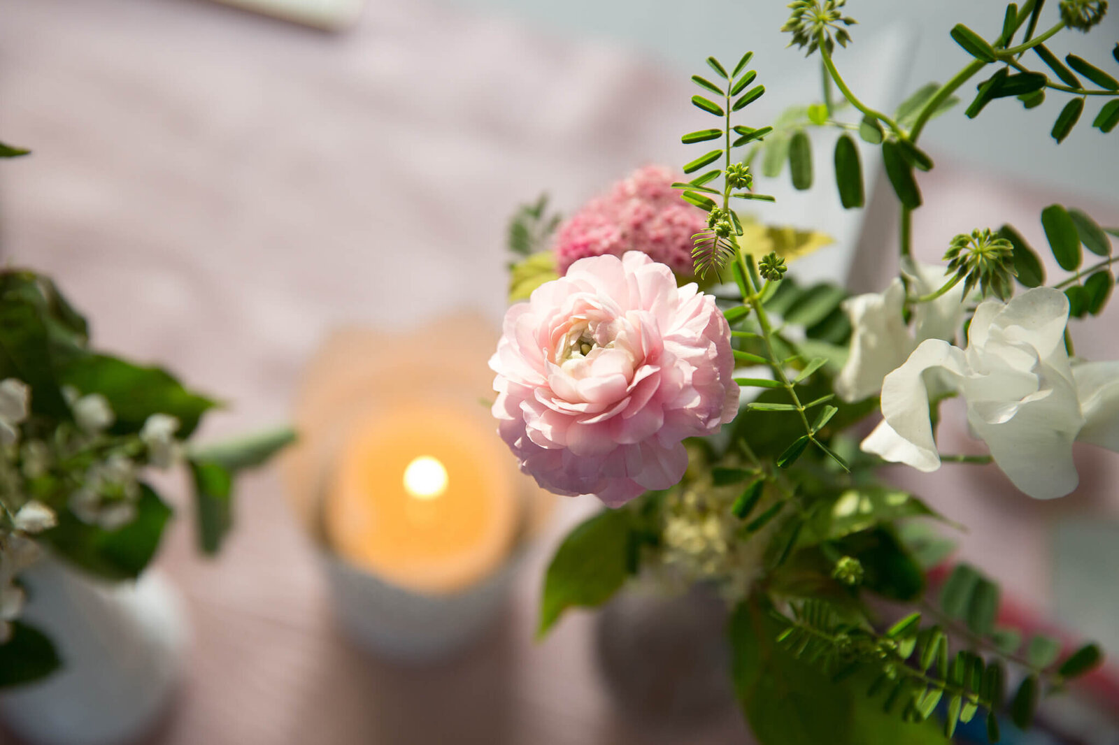 Pink ranunculus flower and candle on table setting for garden wedding.