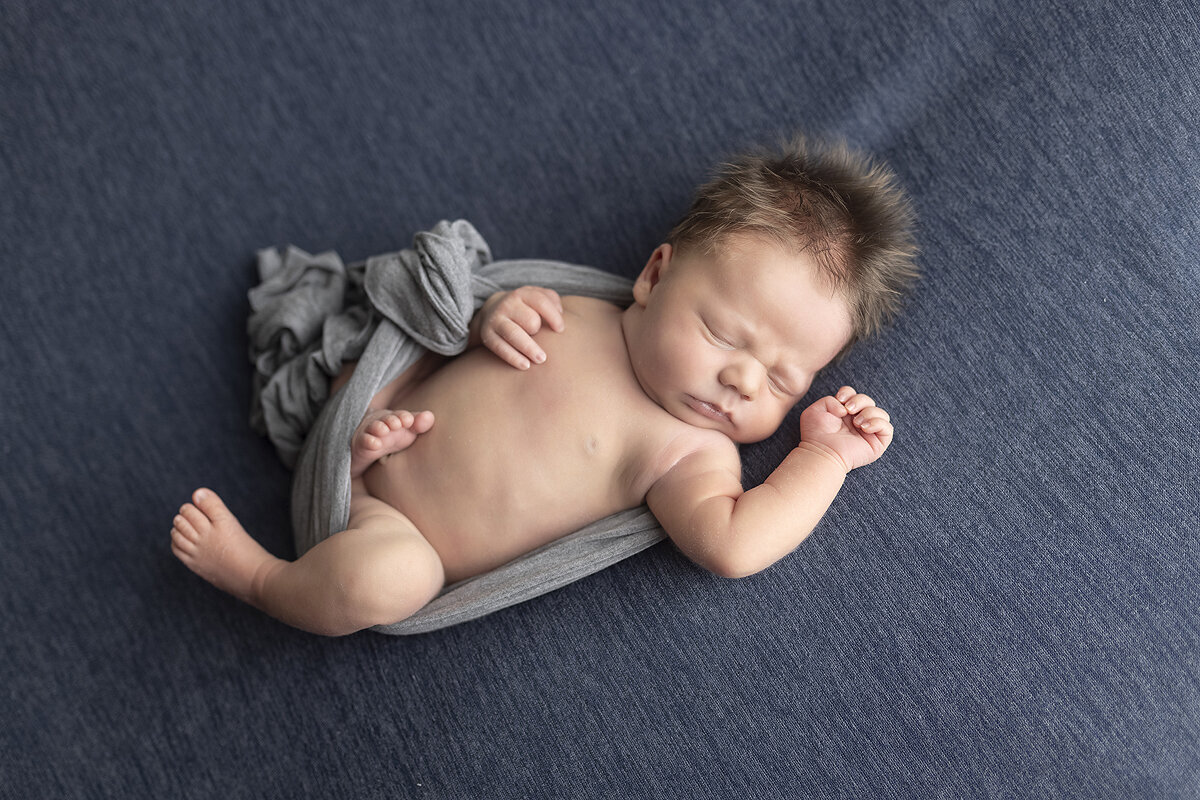 Newborn boy on his back in blue fabric.