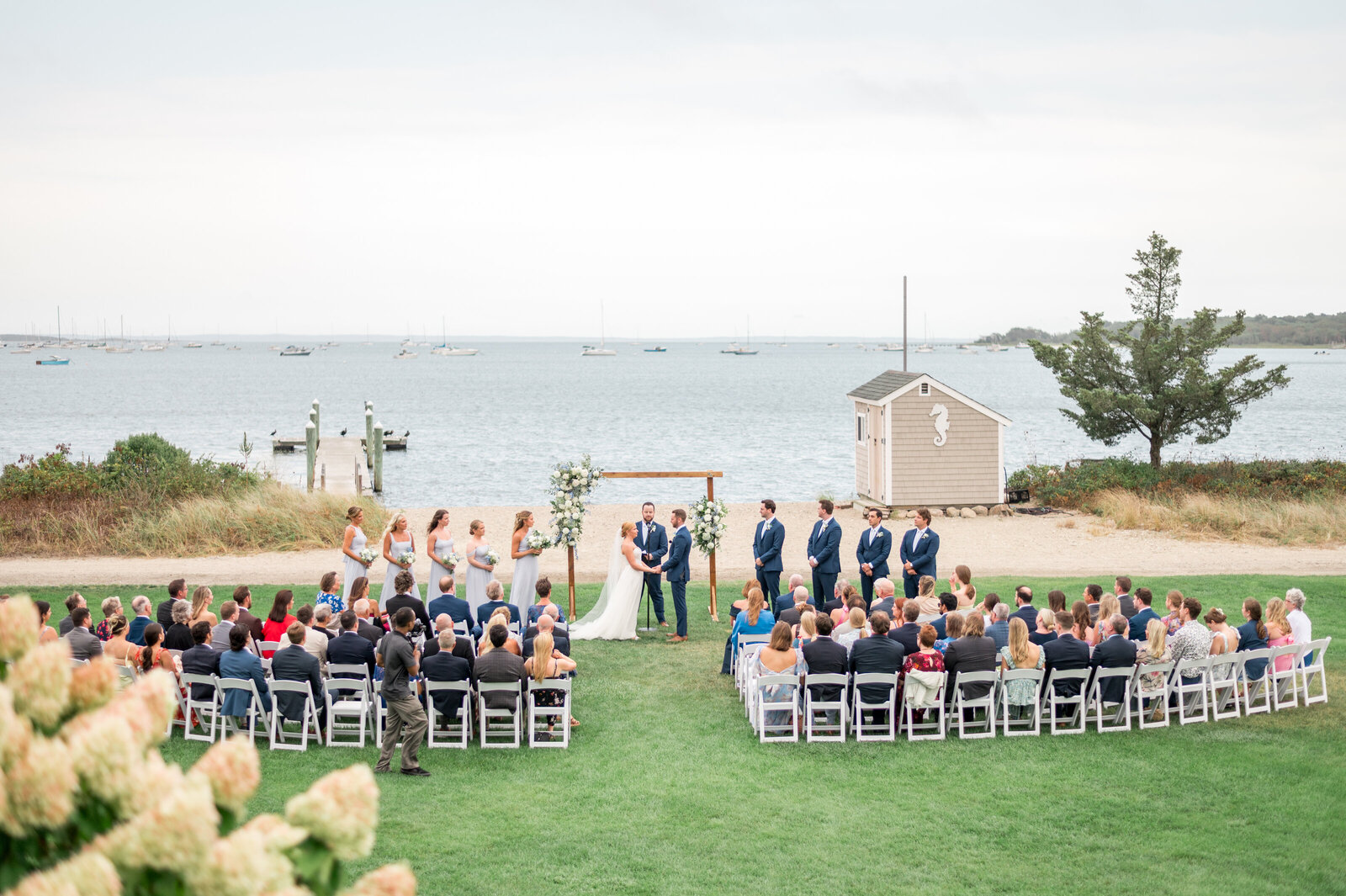 Outdoor waterfront wedding ceremony at Shining Tides overlooking sailboats and harbor — timeless coastal New England wedding photography by Sarah Surette Photography.