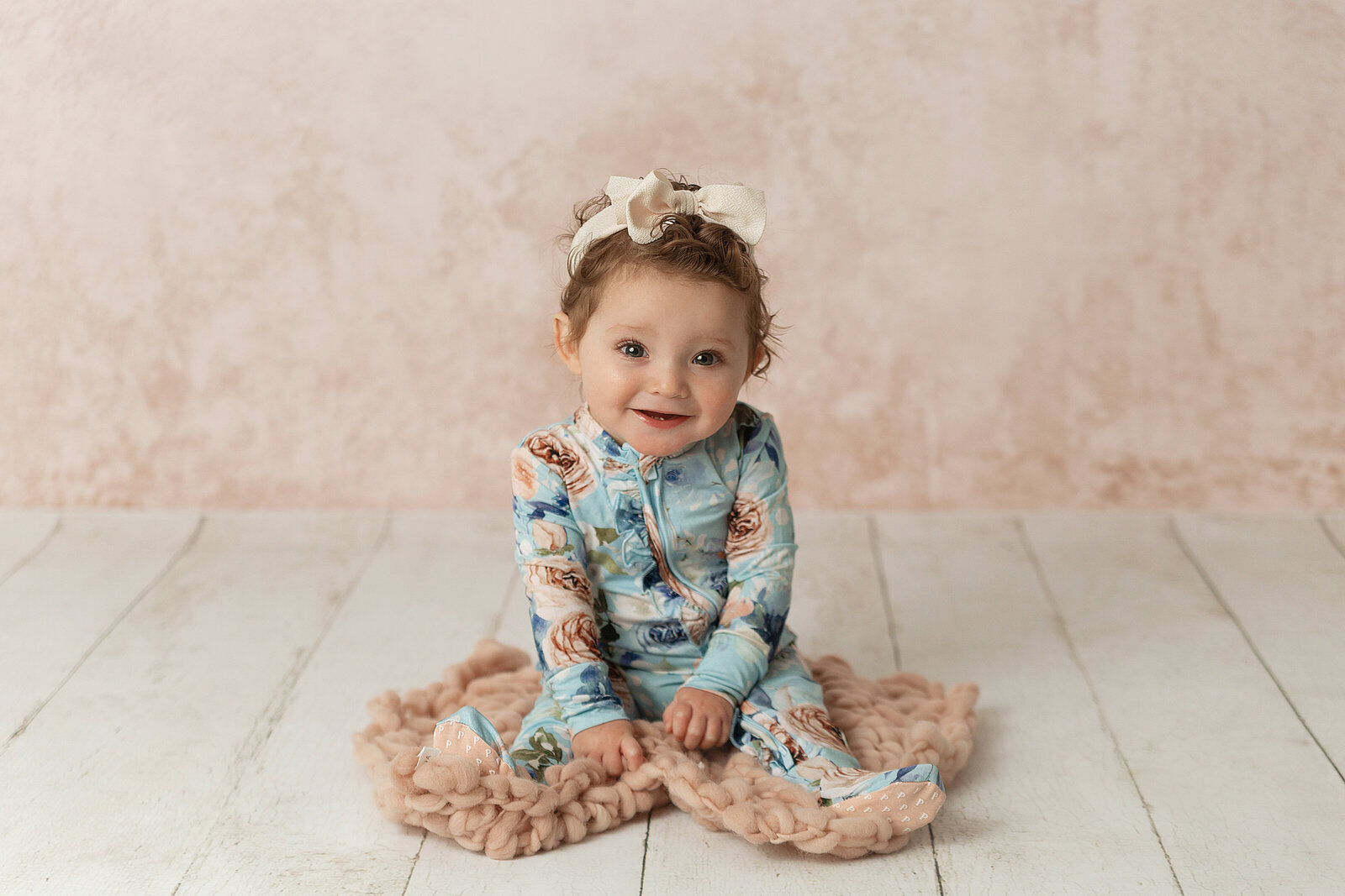 little girl sitting up and smiling for the camera against pink backgroun