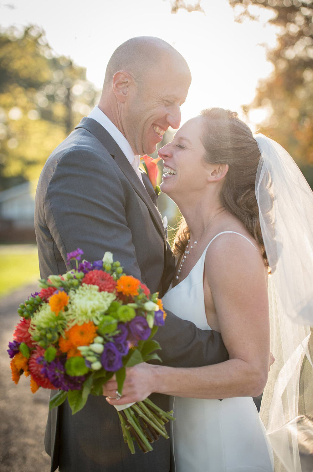 bride and groom hug and laugh in front of sunshine