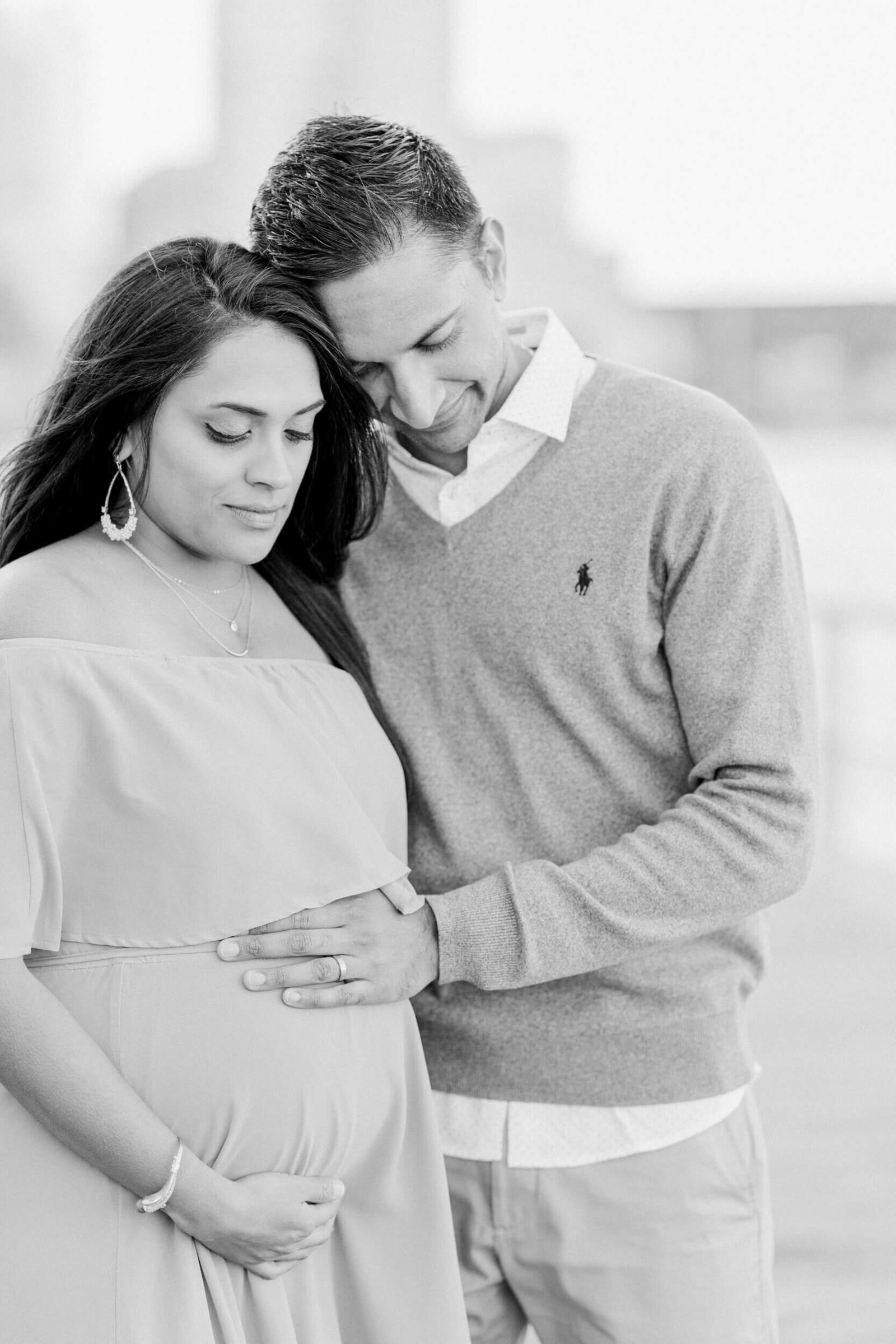 Black and white, pregnant woman and her husband stand close to each other and look down as if reflecting on becoming parents