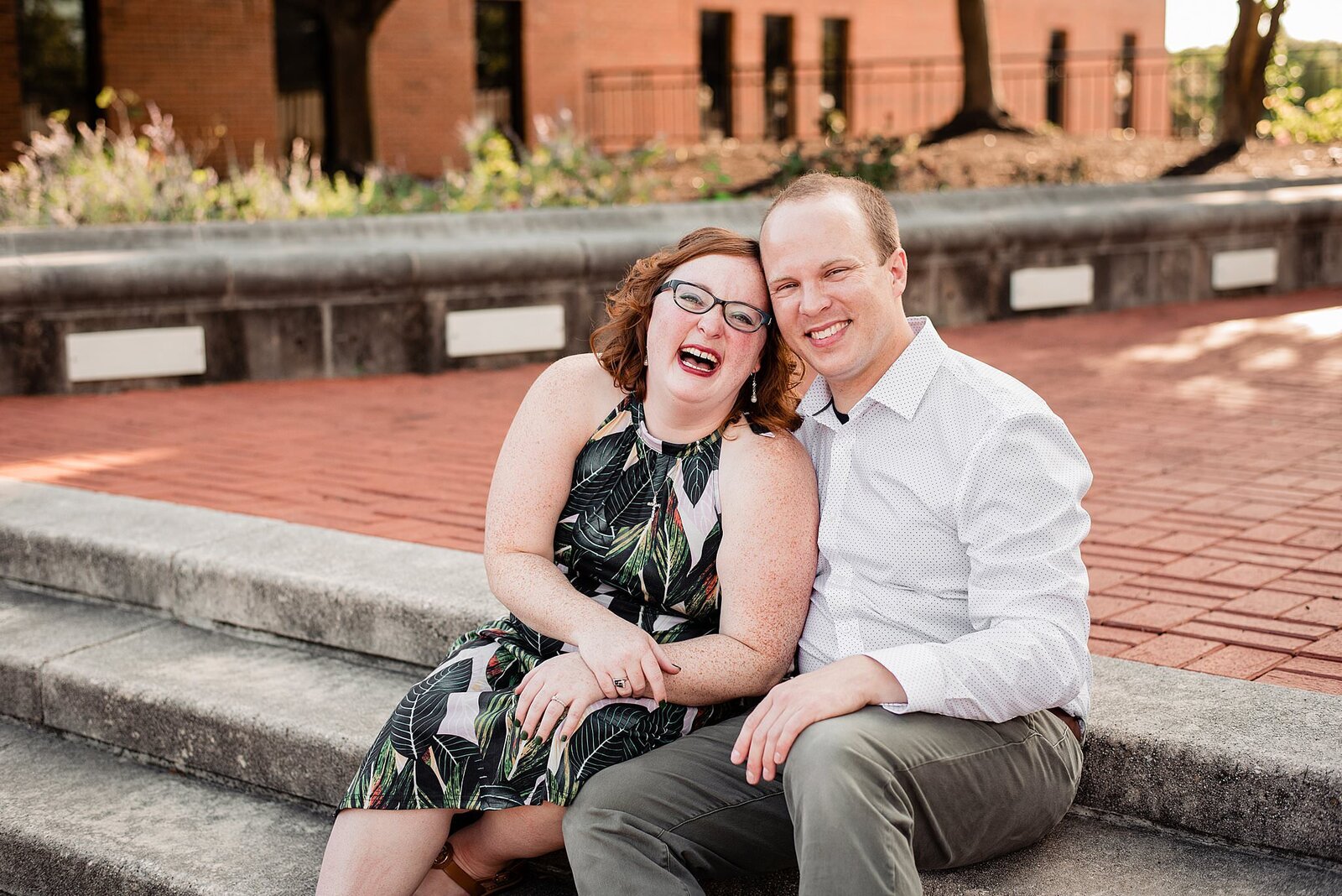 Couple sitting on steps outside of the library smiling and laughing at camera