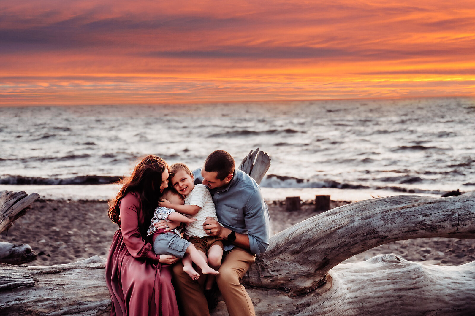 Family of four snuggled on a log with the sunset behind them.