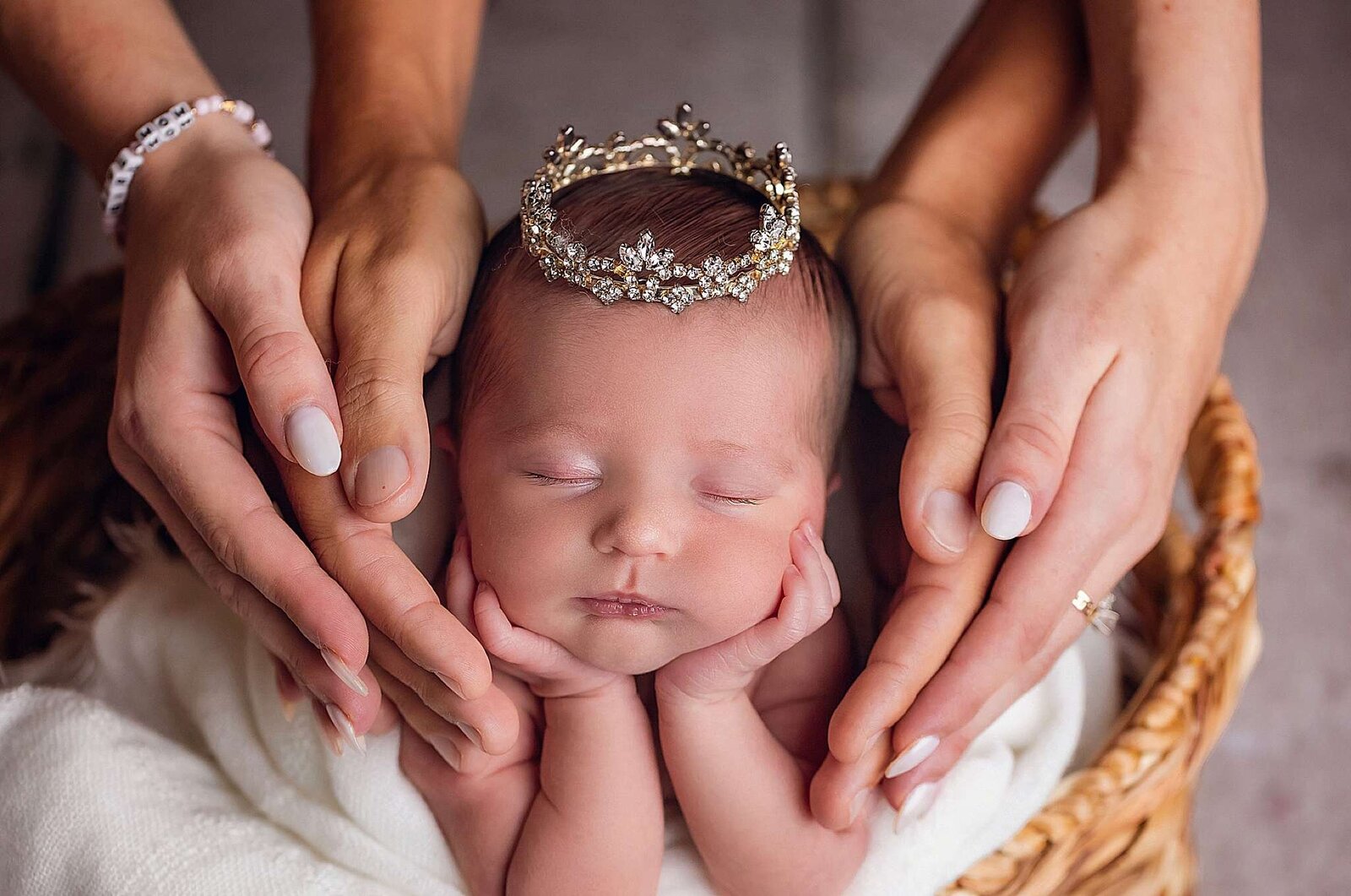 A crowned baby girl is lovingly held by her parents hands, showcasing Bia Schaefer's artistry in Orlando newborn photography.