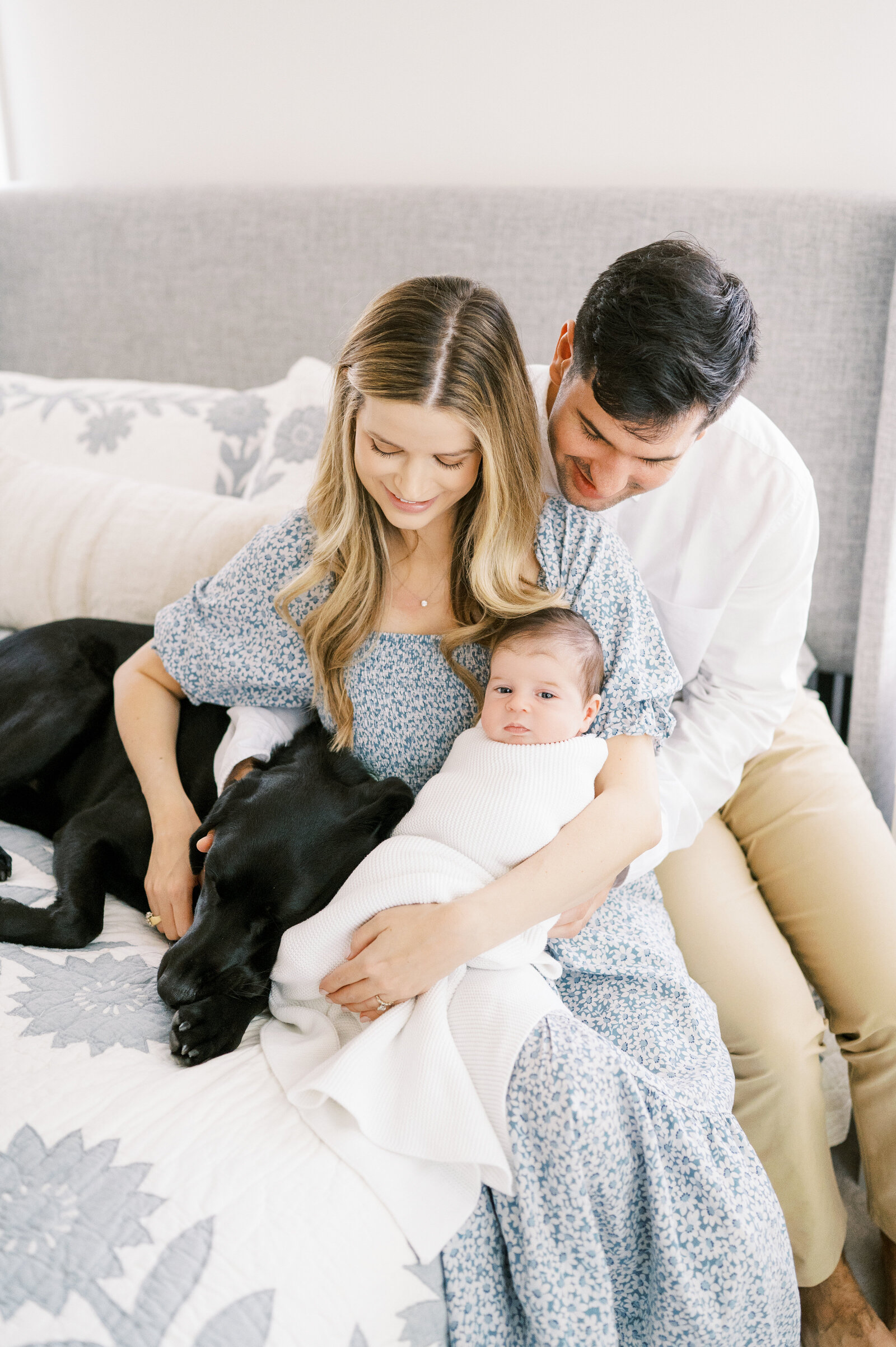 Mom and Dad with newborn baby boy snuggling black dog on the bed during in-home newborn photography session in Raleigh, NC