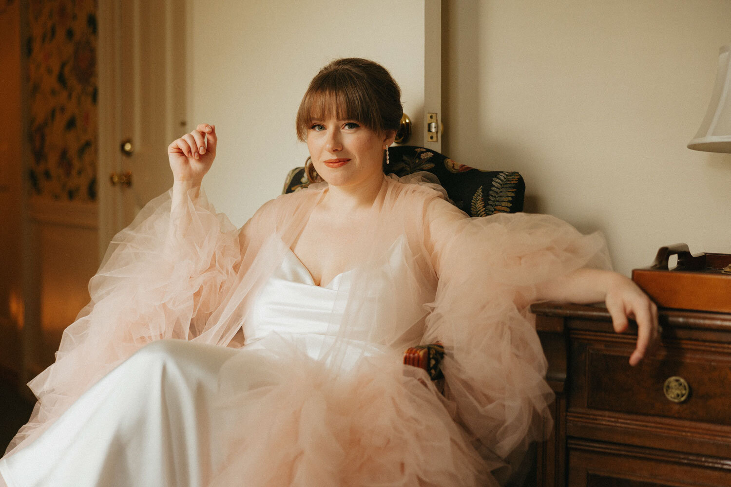 Bride in a light pink robe, sitting in a chair with a soft smile