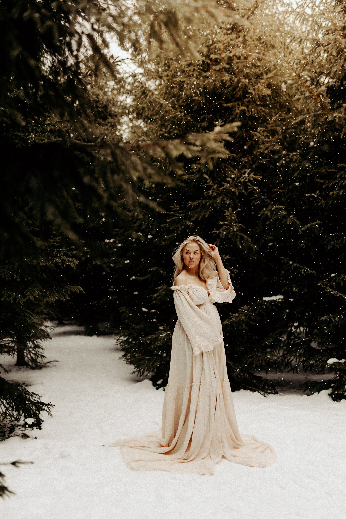 en gravid mamma står i en skog med snö och håller om sin mage