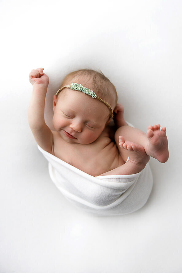 Newborn wrapped in white  sleeps for her photo session.