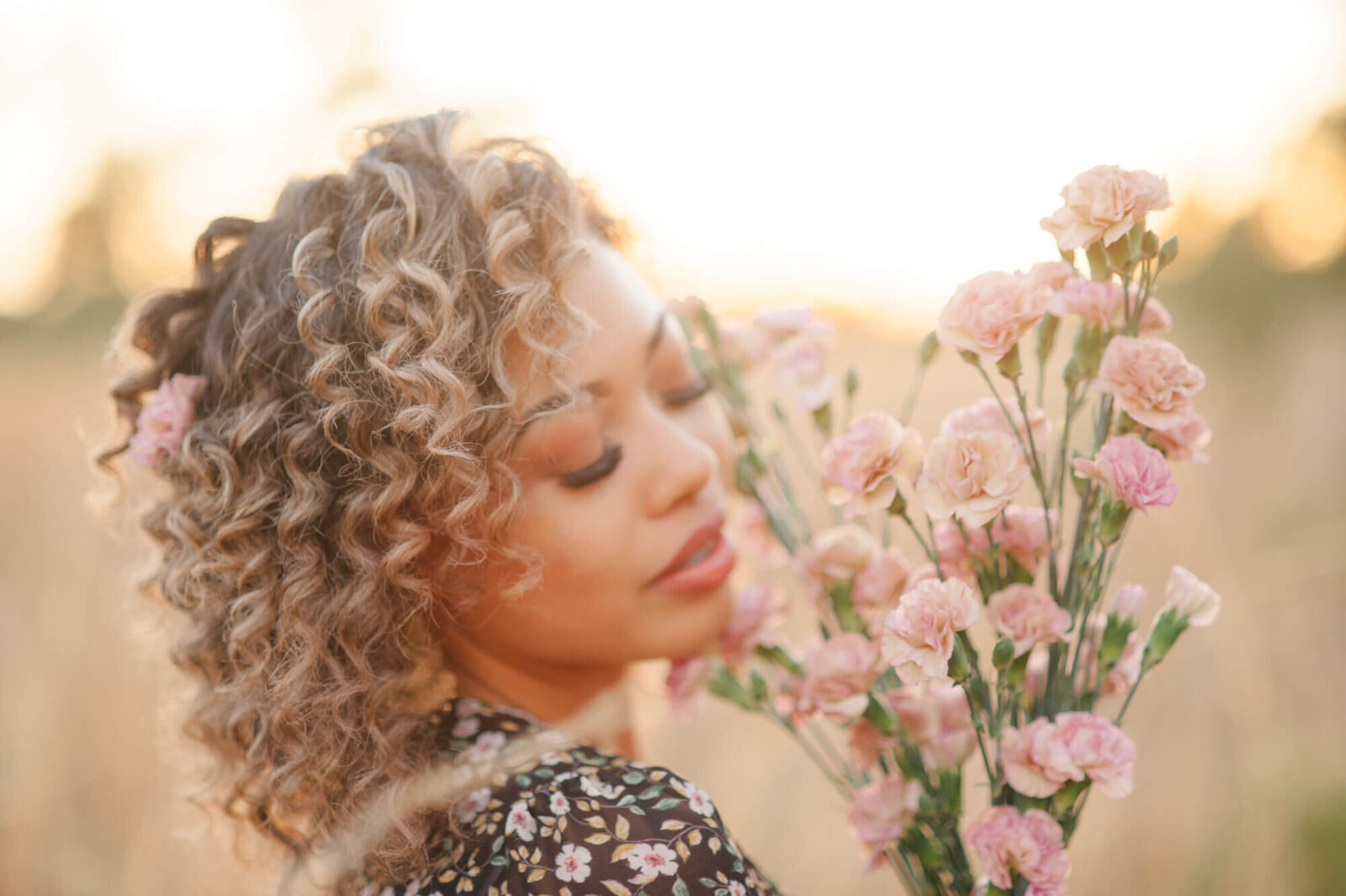 Senior girl holding pink florals with beautiful curly hair at sunset