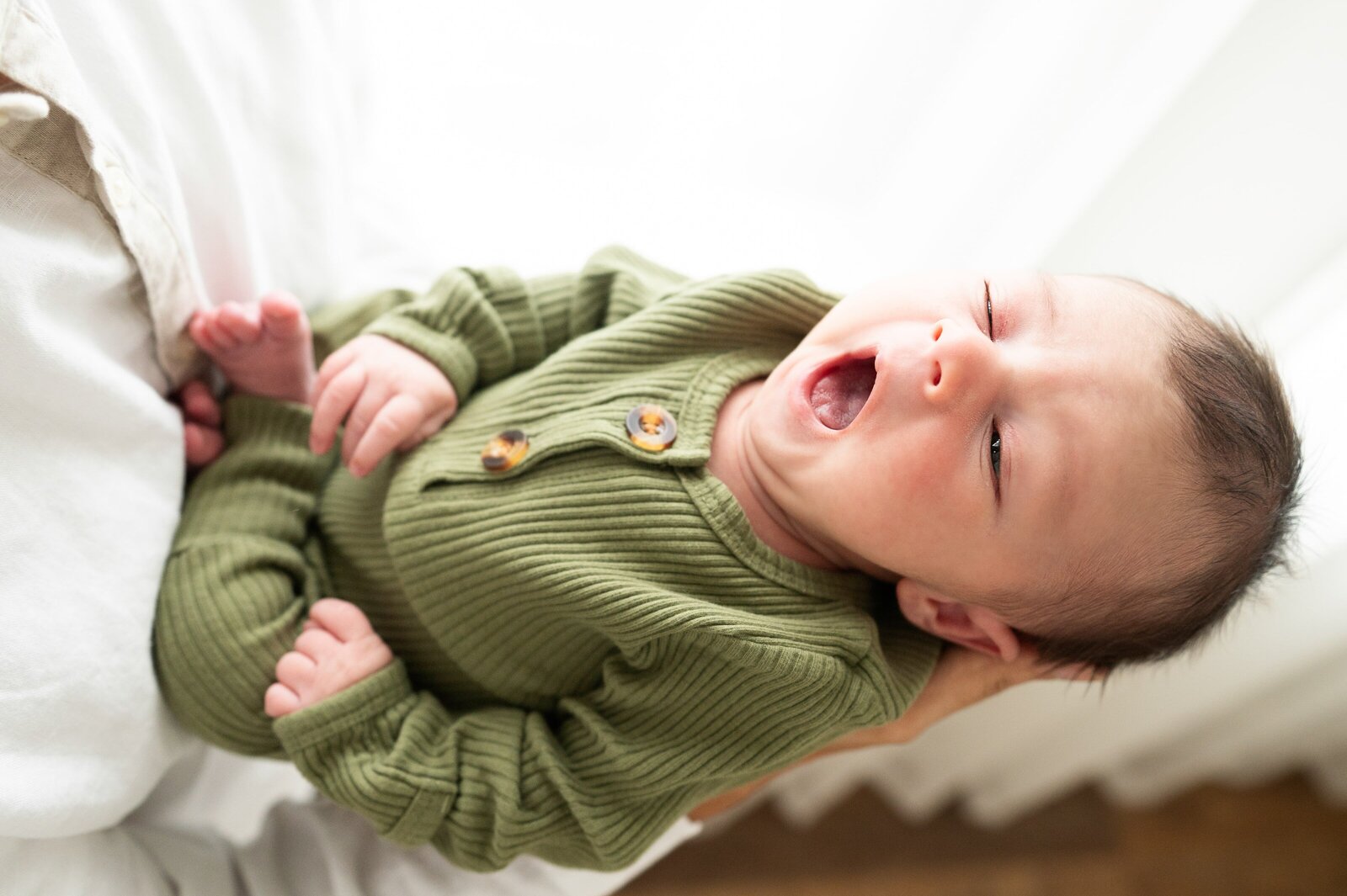 newborn boy in a green onesie yawning