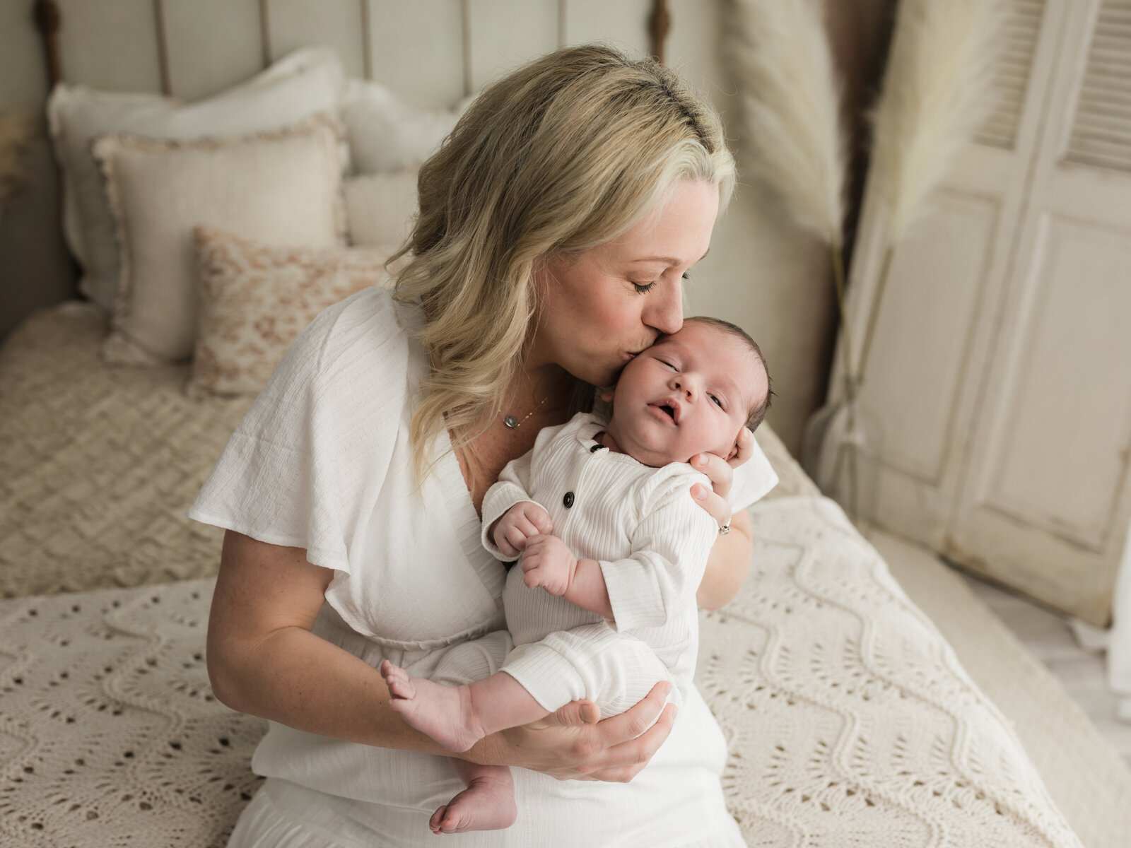 mom holding newborn baby boy in white outfit for studio newborn portraits 