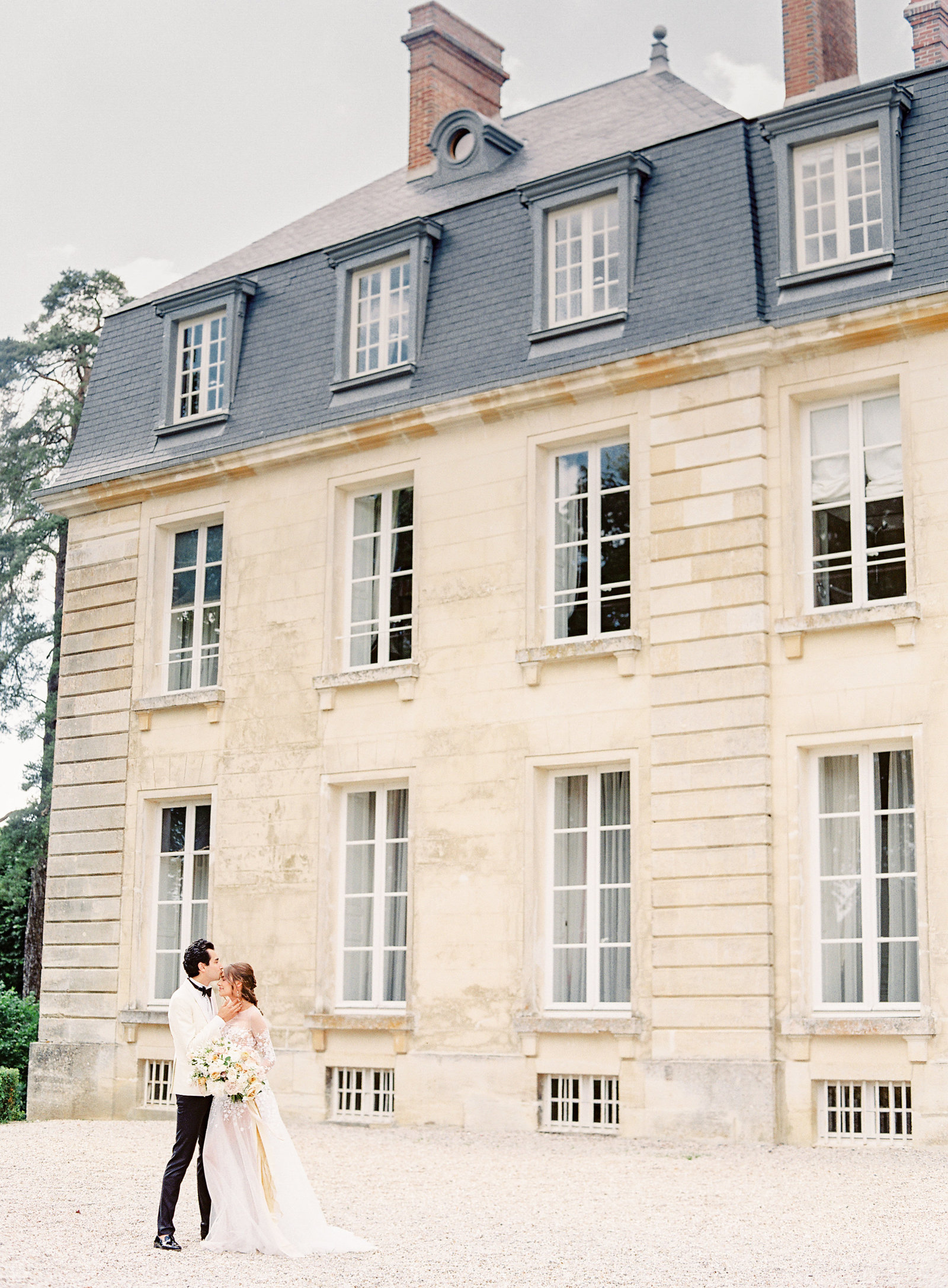 Bride and groom in front of french chateau. Groom kissing bride on forehead. Photographed by Amy Mulder Photography