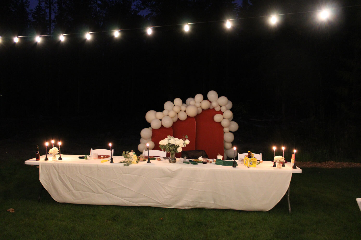 Close-up of a head table with white balloons and candles at night