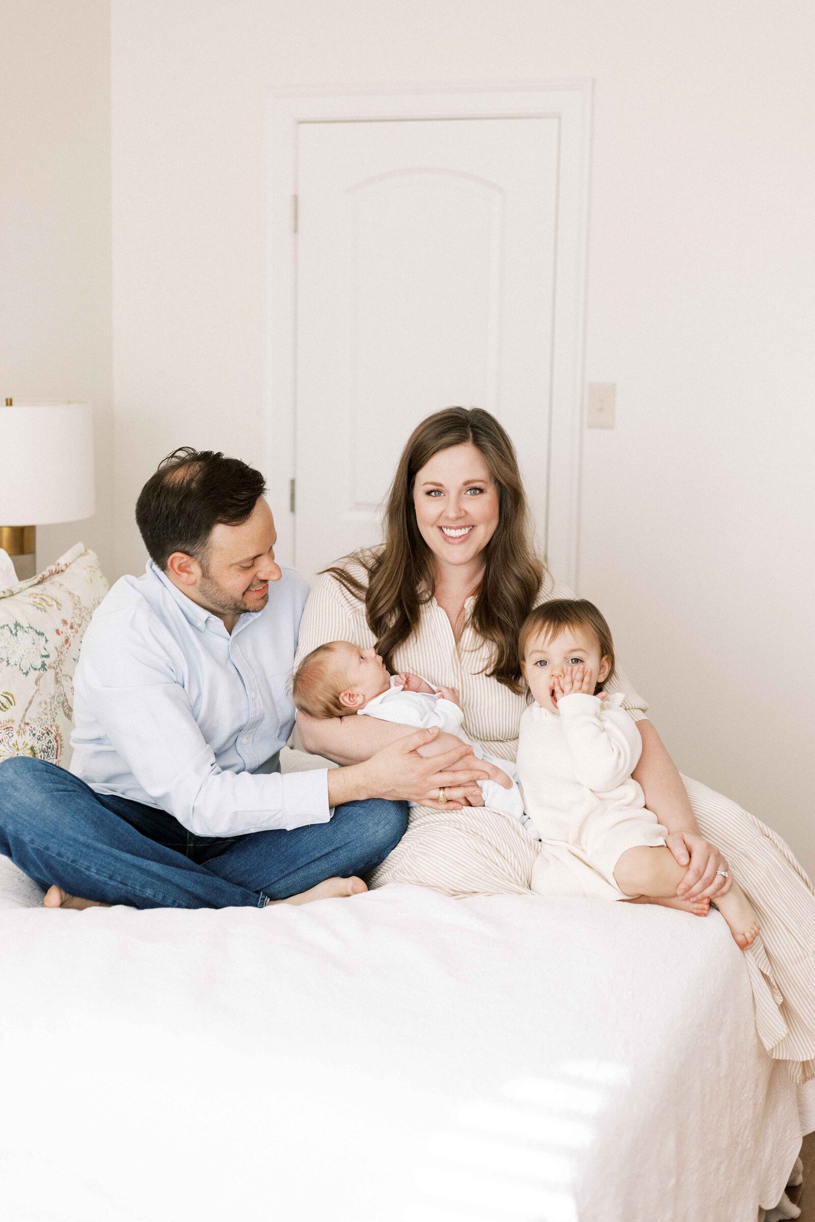 family sitting on bed holding baby during newborn photos in peoria illinois 
