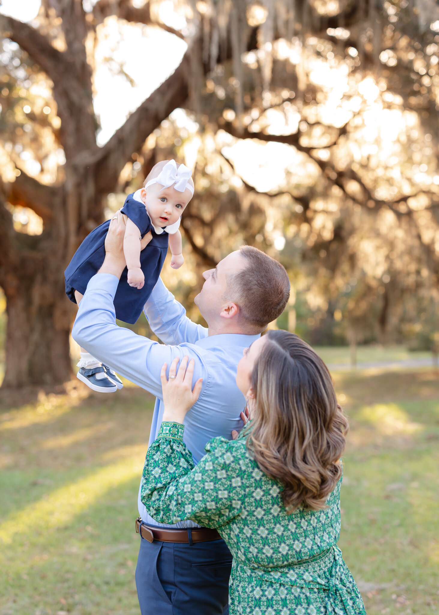 Dad holding daughter into the air and mom is holding dad's arm and everyone is happy.