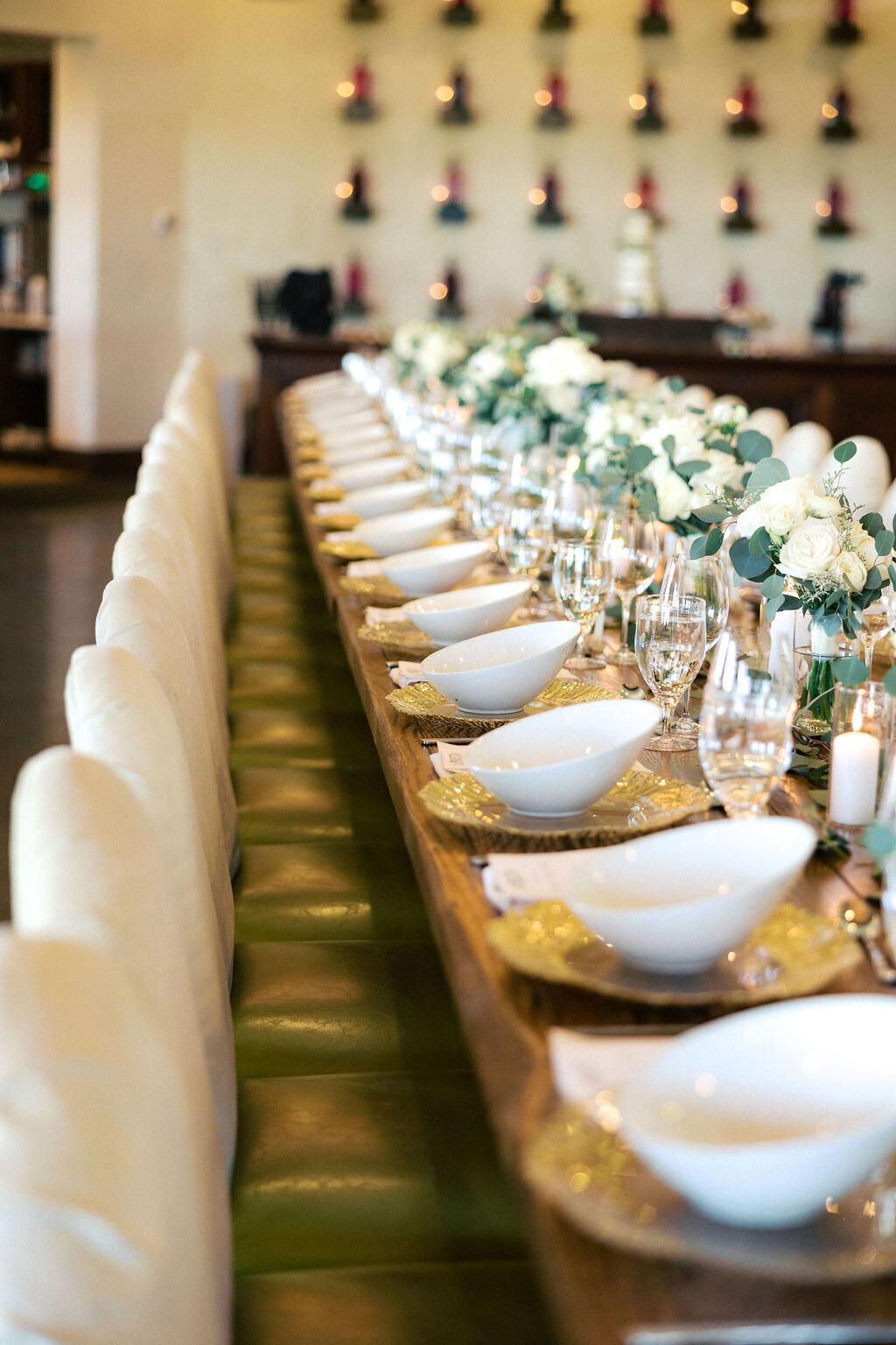 long table at wedding reception with white bowls and floral greens in center