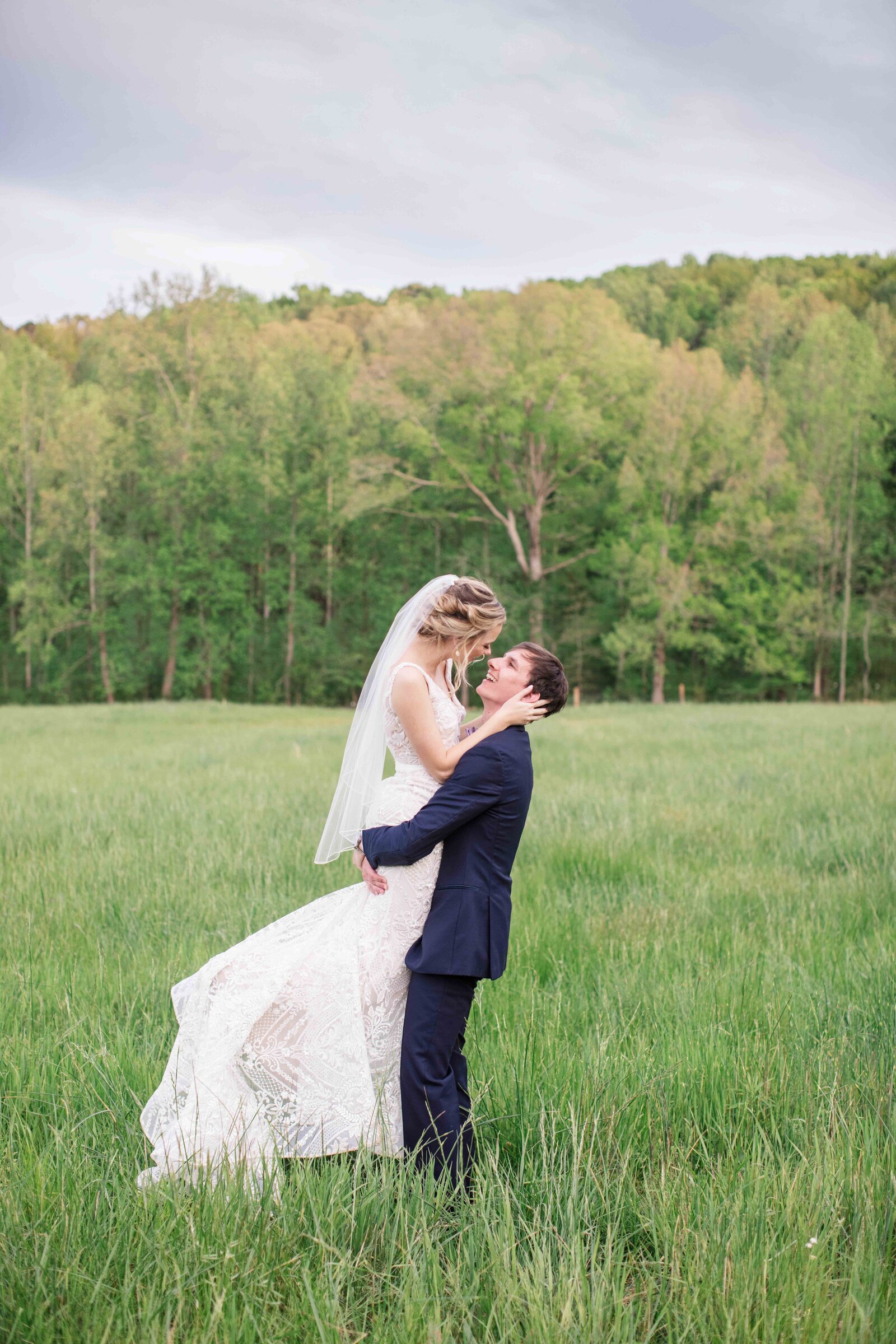 Wedding photographer in Texas captures bride and groom in field as he lifts her in the air at sunset portrait