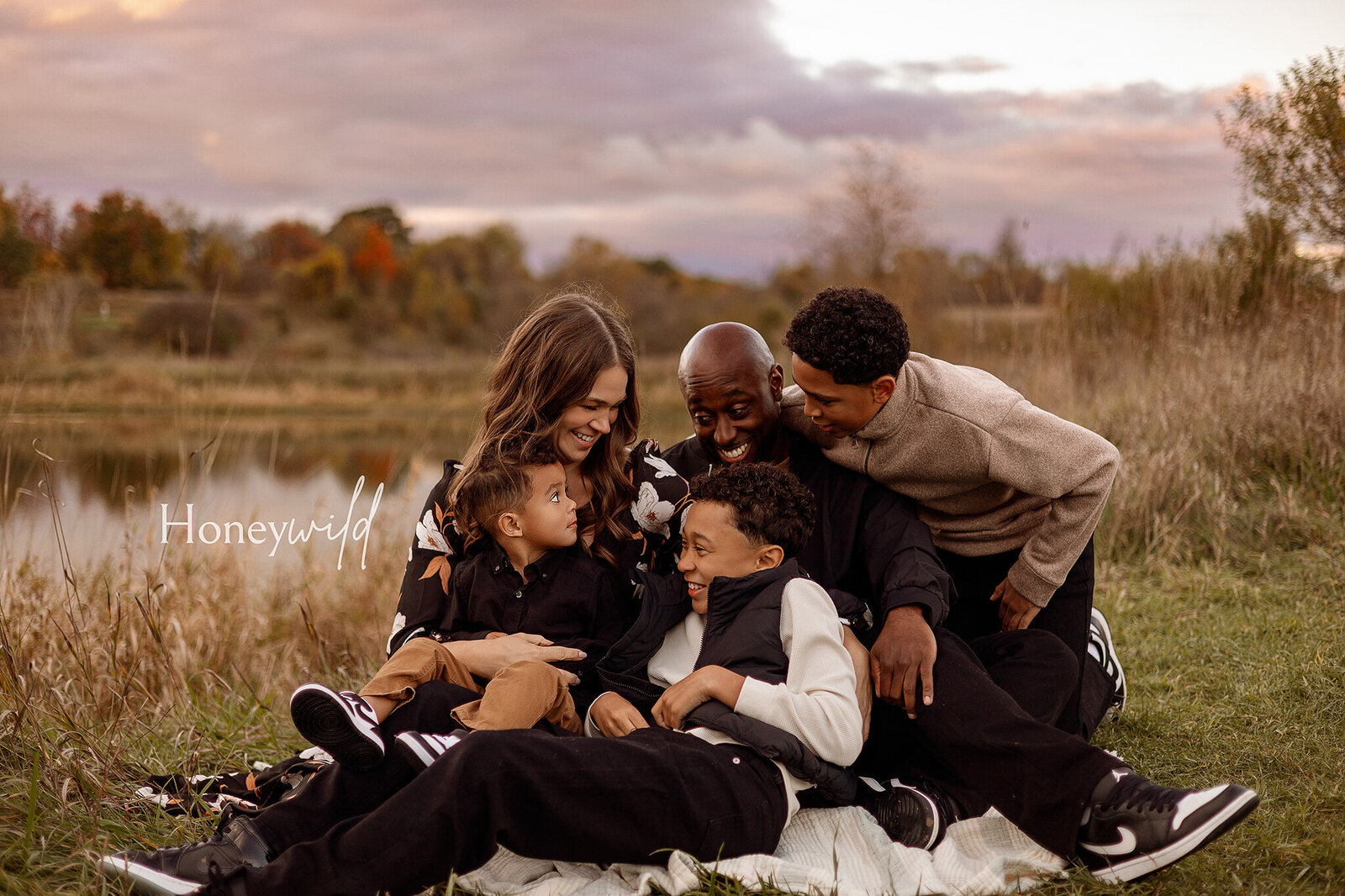 A family of three walking through a scenic grassy field in Grand Rapids, Michigan, during a golden-hour family photography session, capturing natural and joyful moment