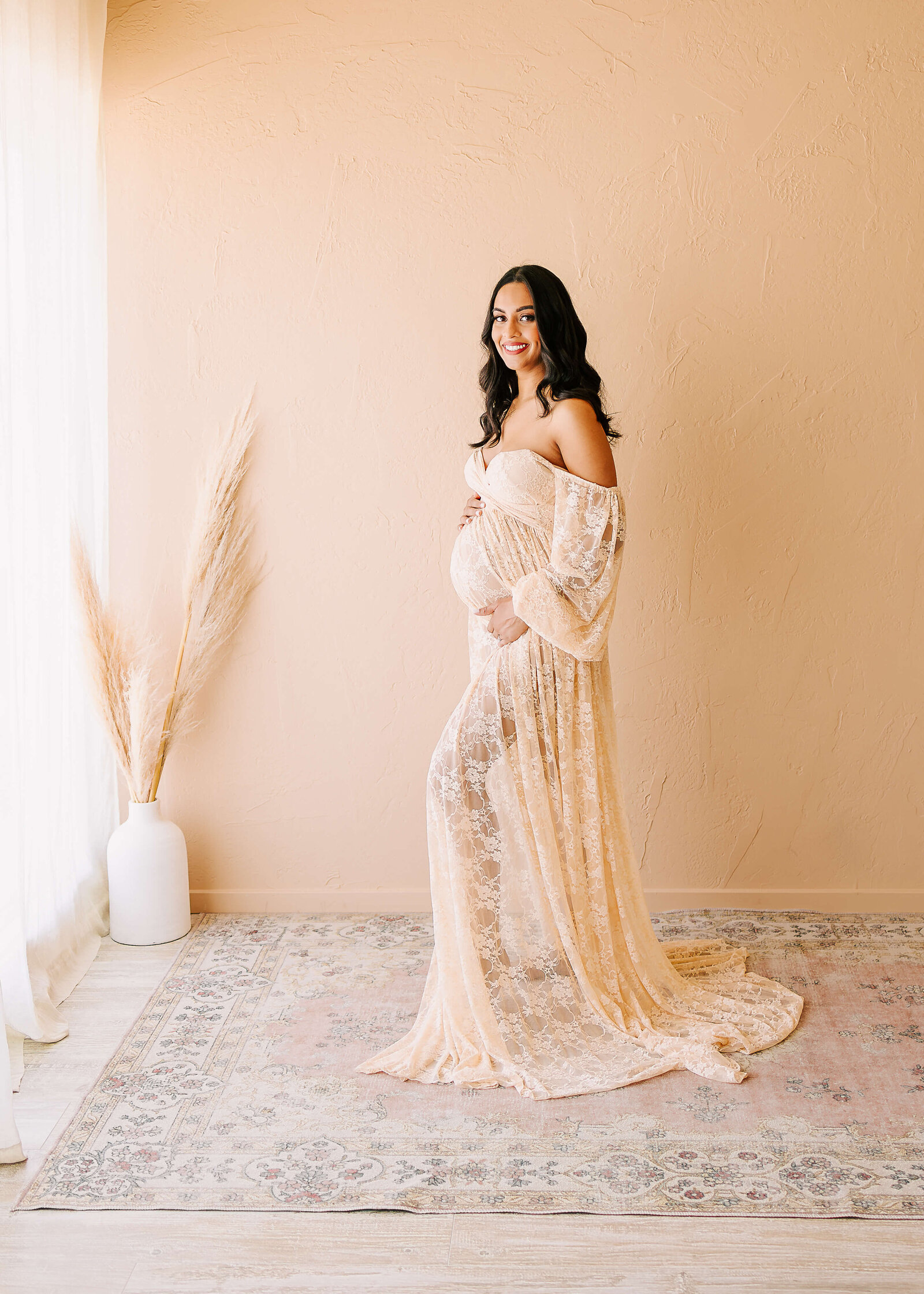 Expectant mom posed in boho studio in Huntington Beach wearing lace gown by Ashley Nicole Photography.