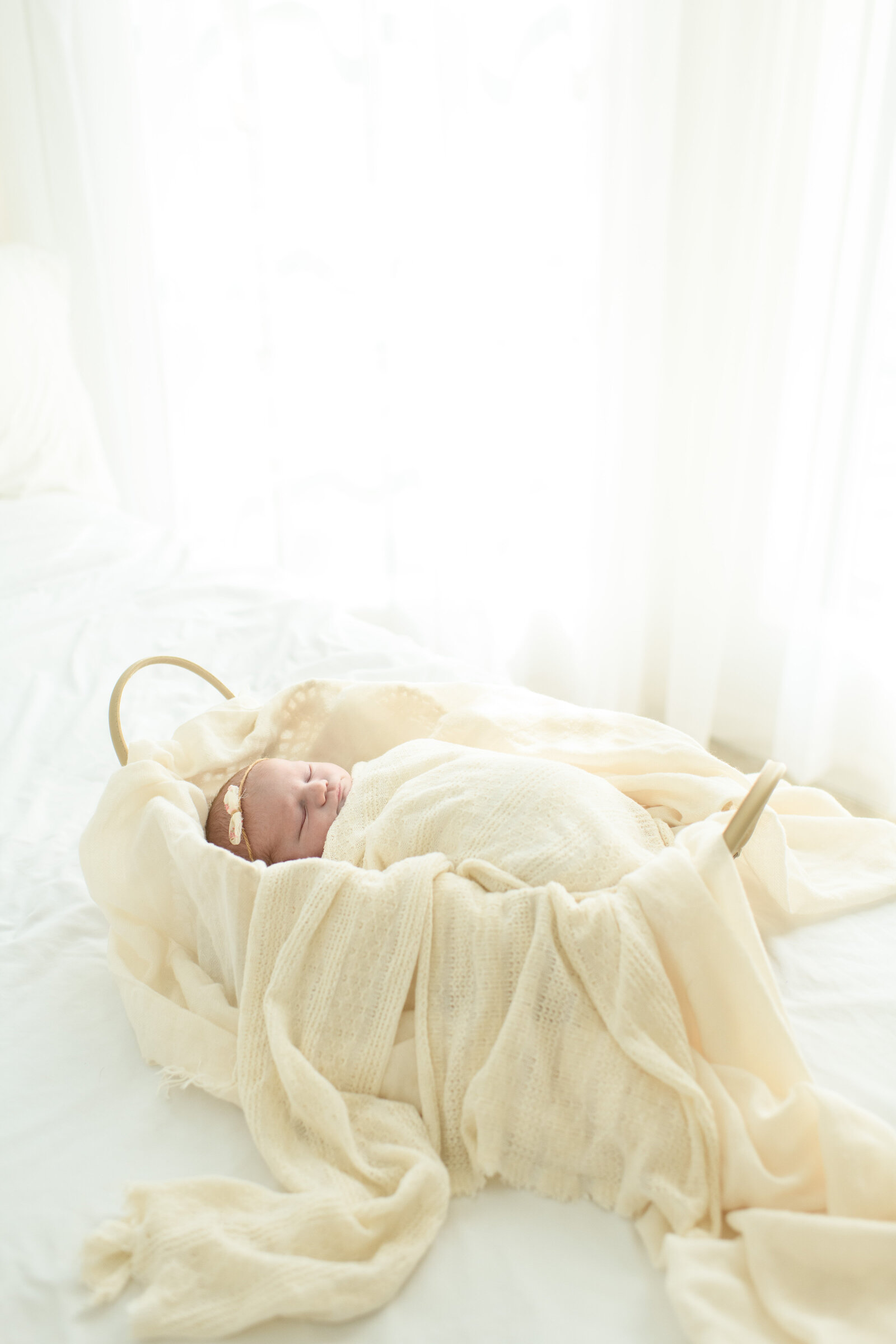  Newborn baby sleeps peacefully in a bassinet wrapped in a cozy white blanket. A timeless newborn session by Moments in Light Photography.