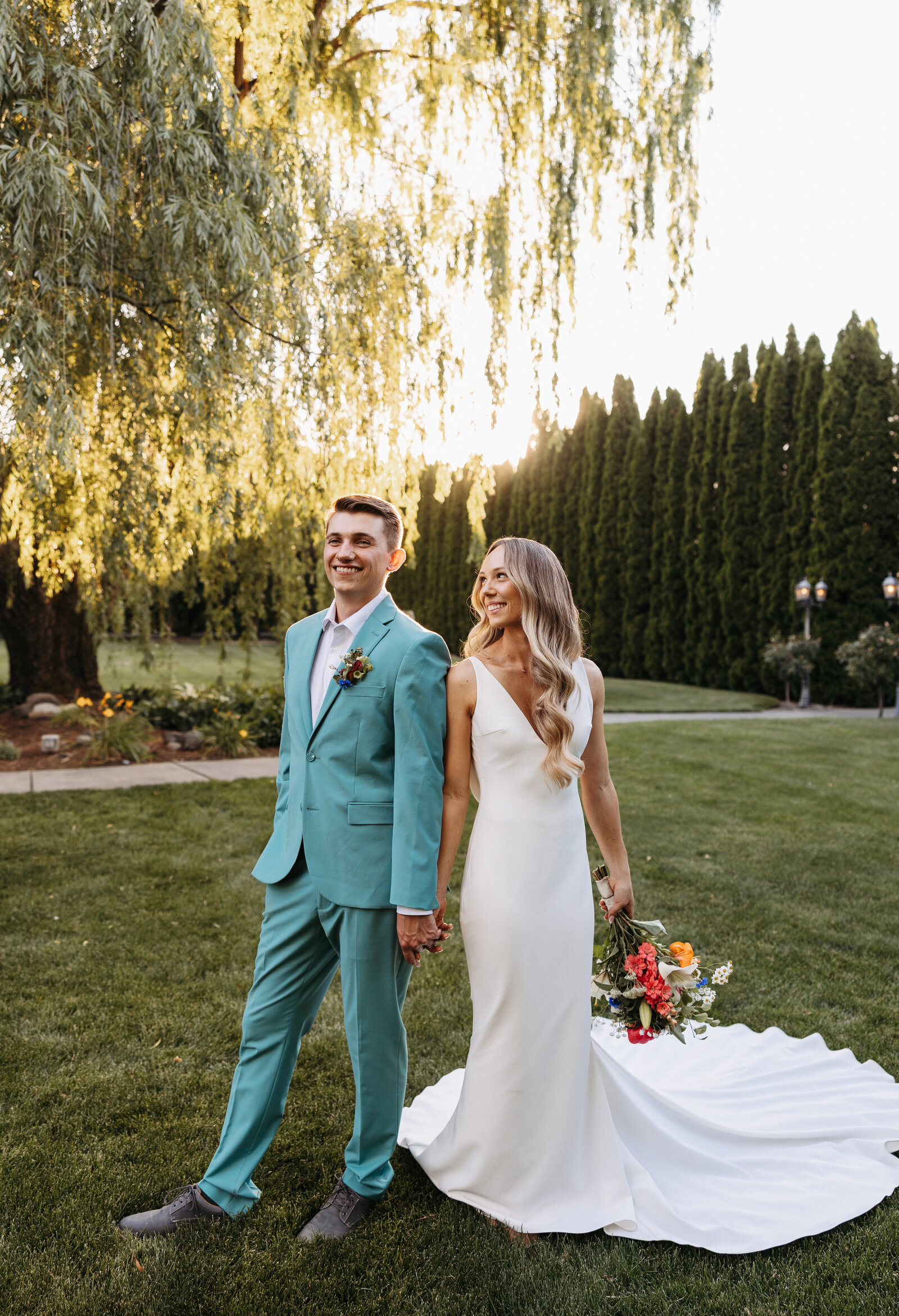 bride and groom stand under a willow tree at their garden wedding