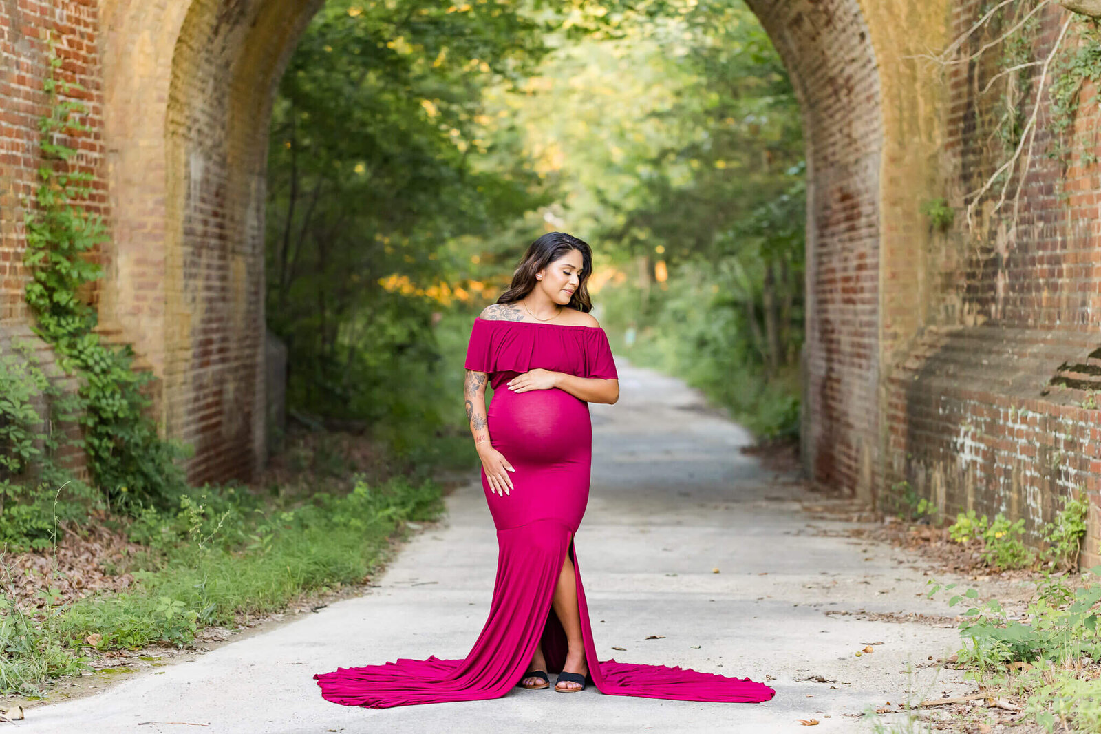 A mother-to-be posing in a red dress and holding her belly.