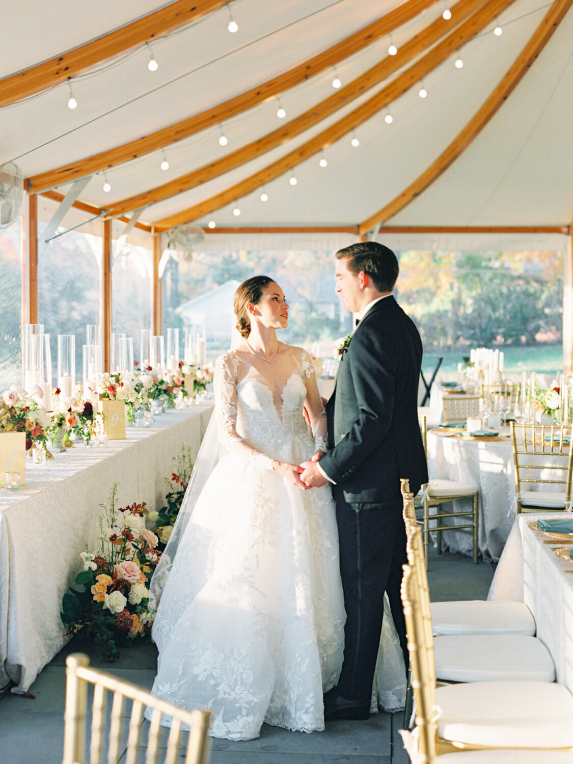 A bride and groom share a private moment under a sailcloth tent with luxury tables around them.