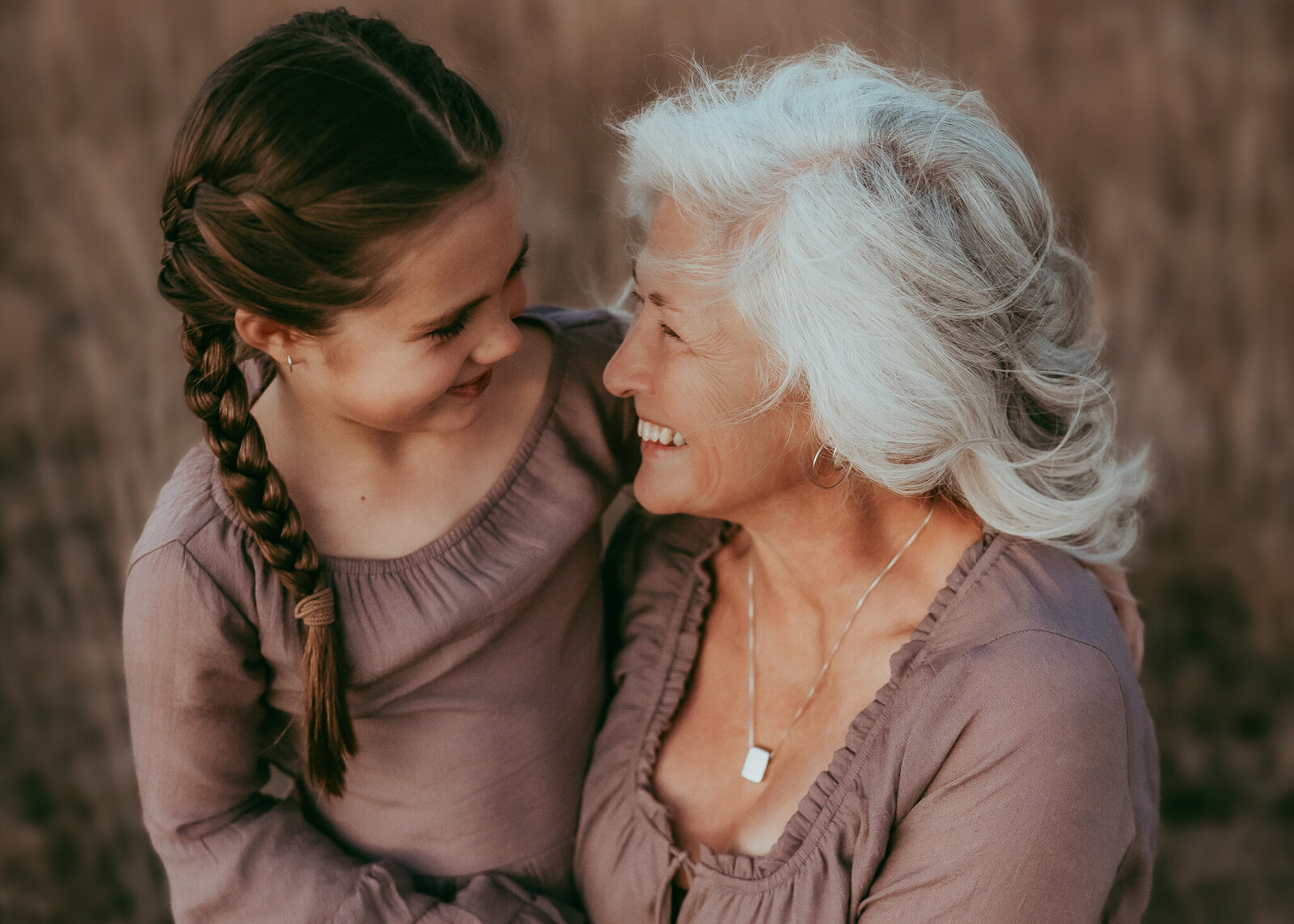 A granddaughter sits on her grandma's lap as they giggle at each other, while the sunsets painting their faces with beautiful light.