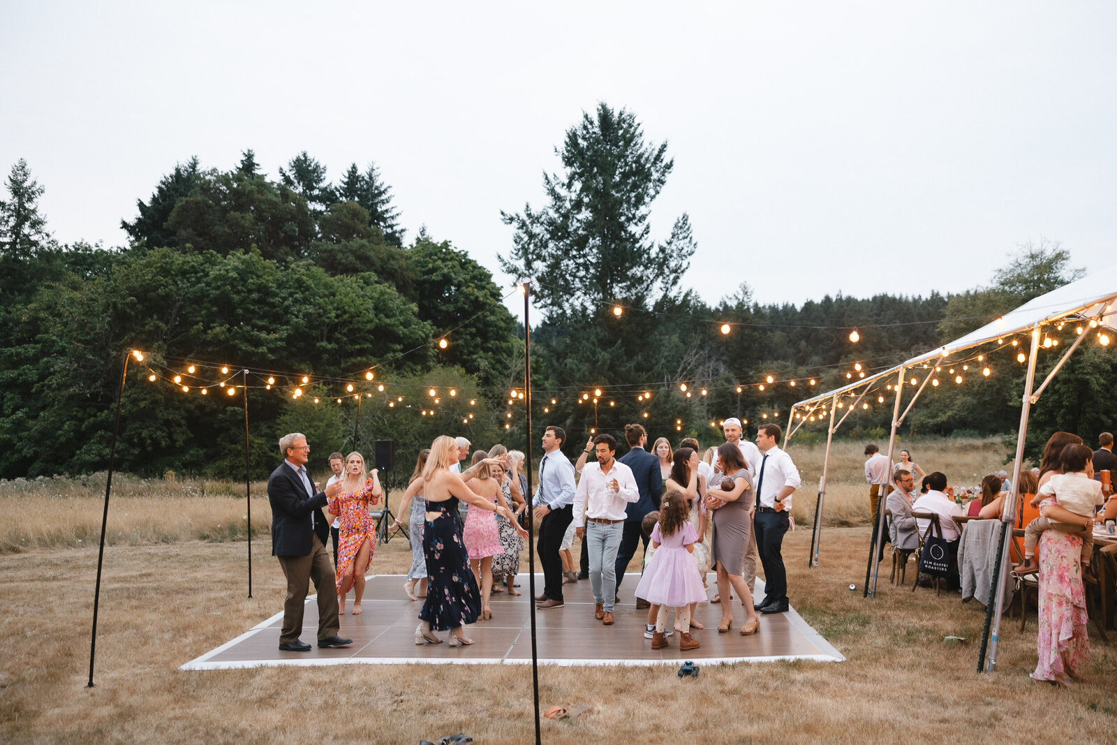 Wedding guests dancing on an outdoor dance floor with cafe string lights.