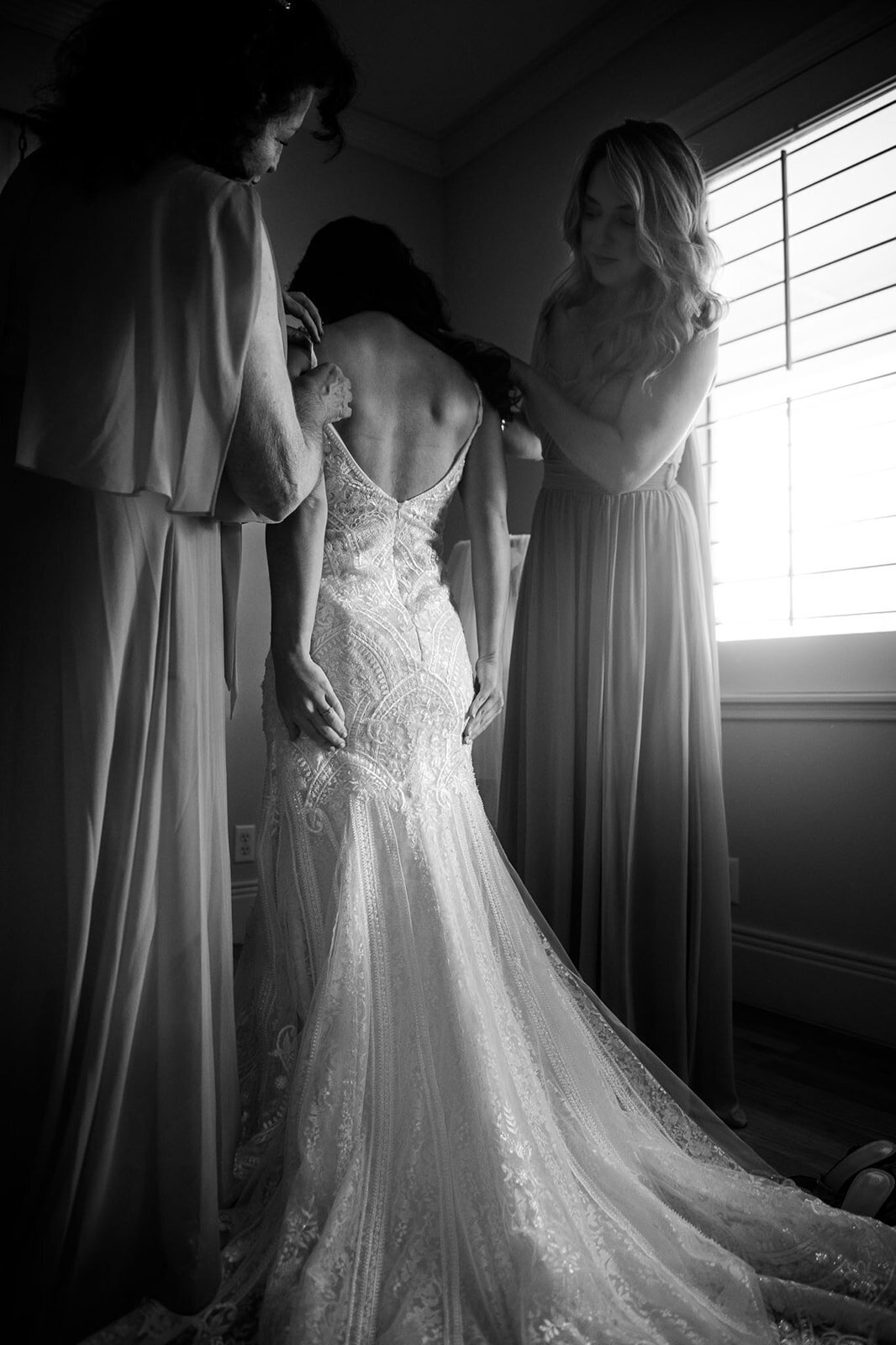 A touching black-and-white moment of a bride being helped into her wedding dress by her family before the ceremony. Captured by CMH Studios, a luxury wedding photographer in San Antonio