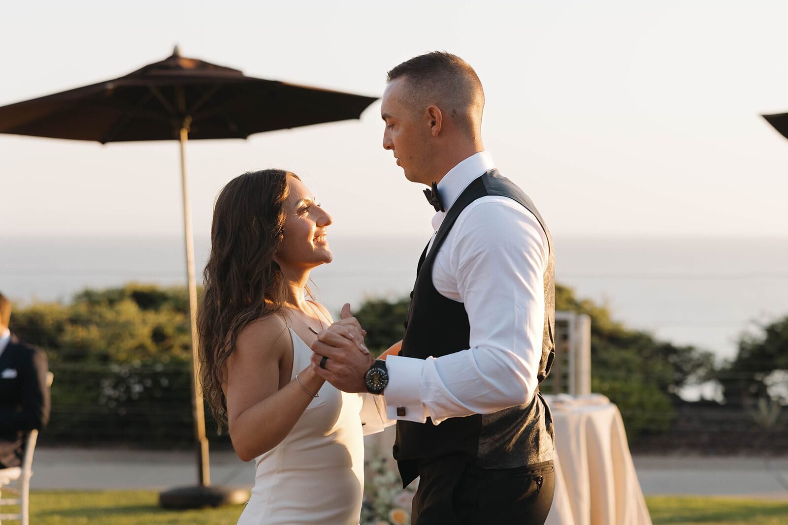 Bride and groom laughing during their first dance with the ocean behind them