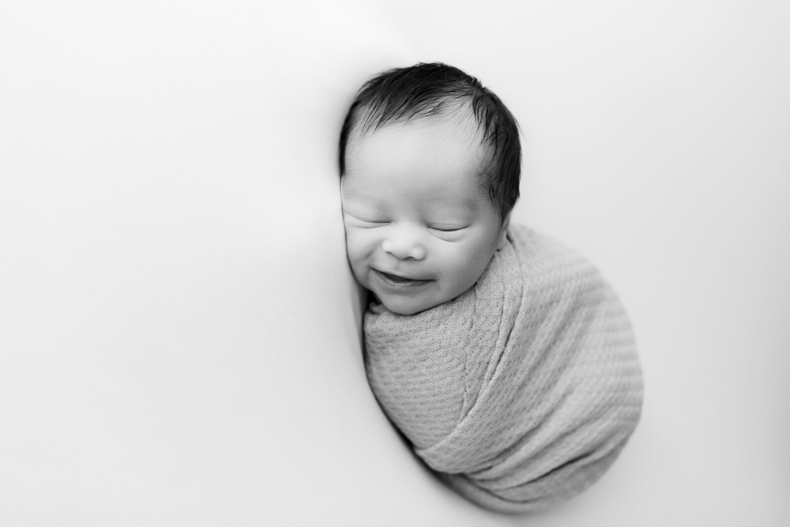 Newborn baby smiles while wrapped up in a studio near Birmingham