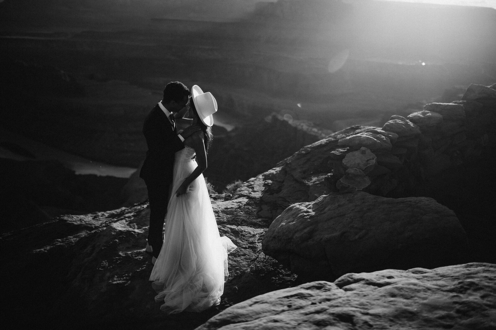 Black and white photo of bride and groom on top of desert canyon at sunset