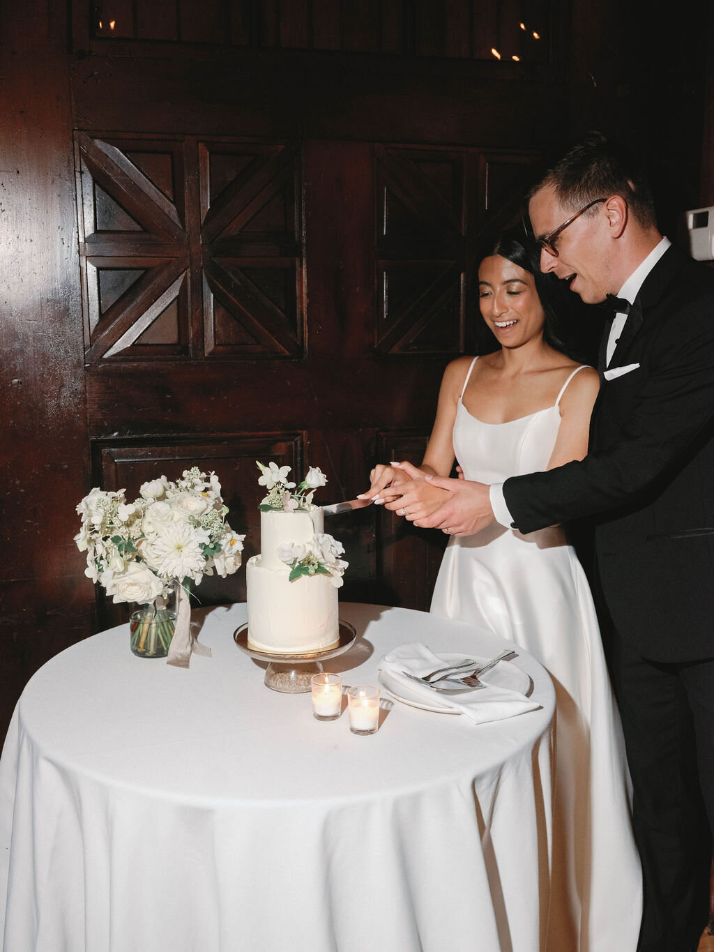 Bride and groom cutting the two-tiered white cake with white floral accents.
