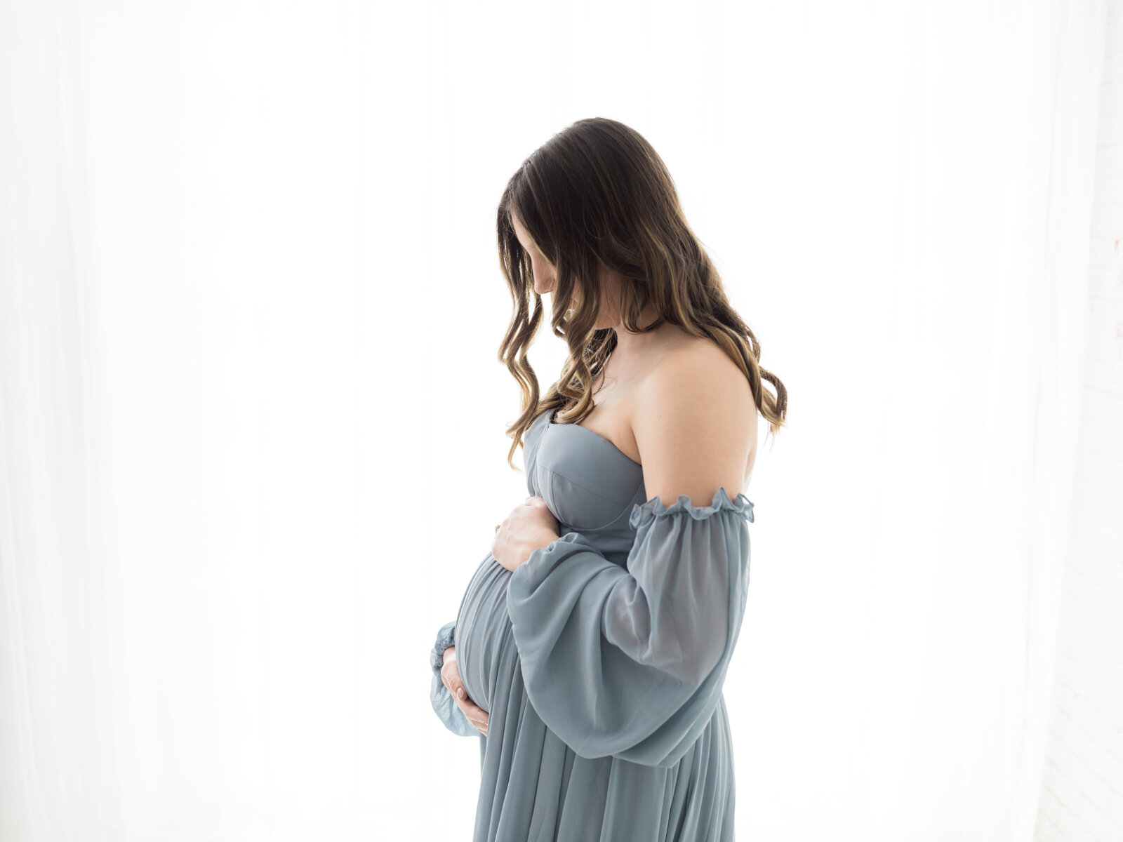 pregnant mother in blue maternity gown holding baby bump for studio portraits cleveland maternity photographer