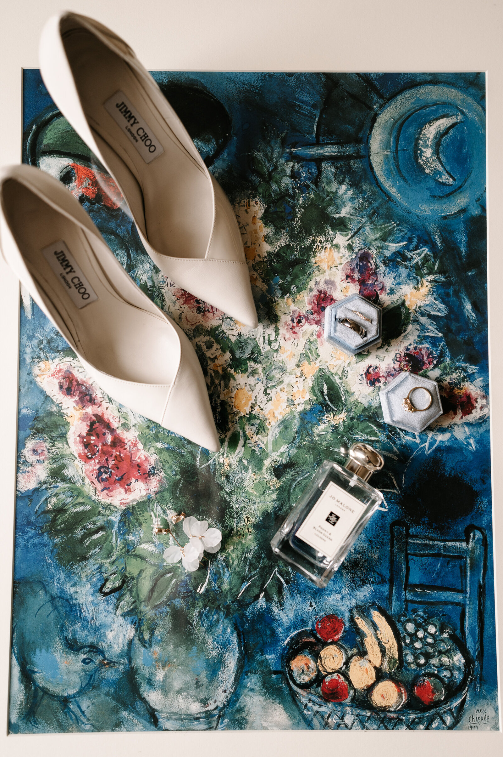 Flat lay image of a bride's wedding shoes, rings, earrings, and perfume